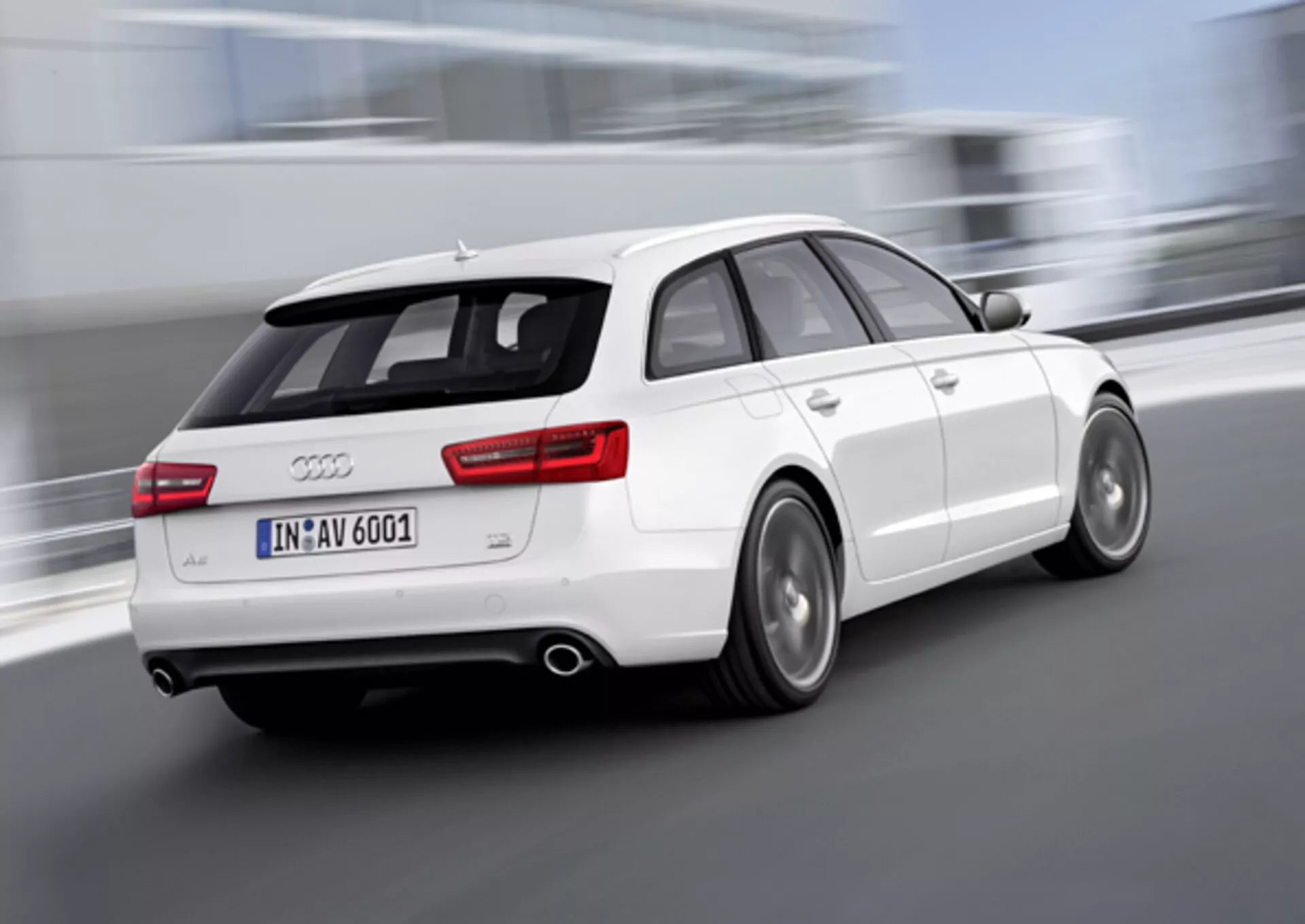 Dynamiczny trzy-czwarty widok z tyłu białego Audi A6 Avant z 2011 roku w ruchu, z rozmytymi kołami wskazującymi na szybkość, podwójnym wydechem, aluminiowymi kołami z widocznymi tarczami hamulcowymi i spojlerem dachowym zwiększającym aerodynamikę, zdjęcie wykonane na zewnątrz.