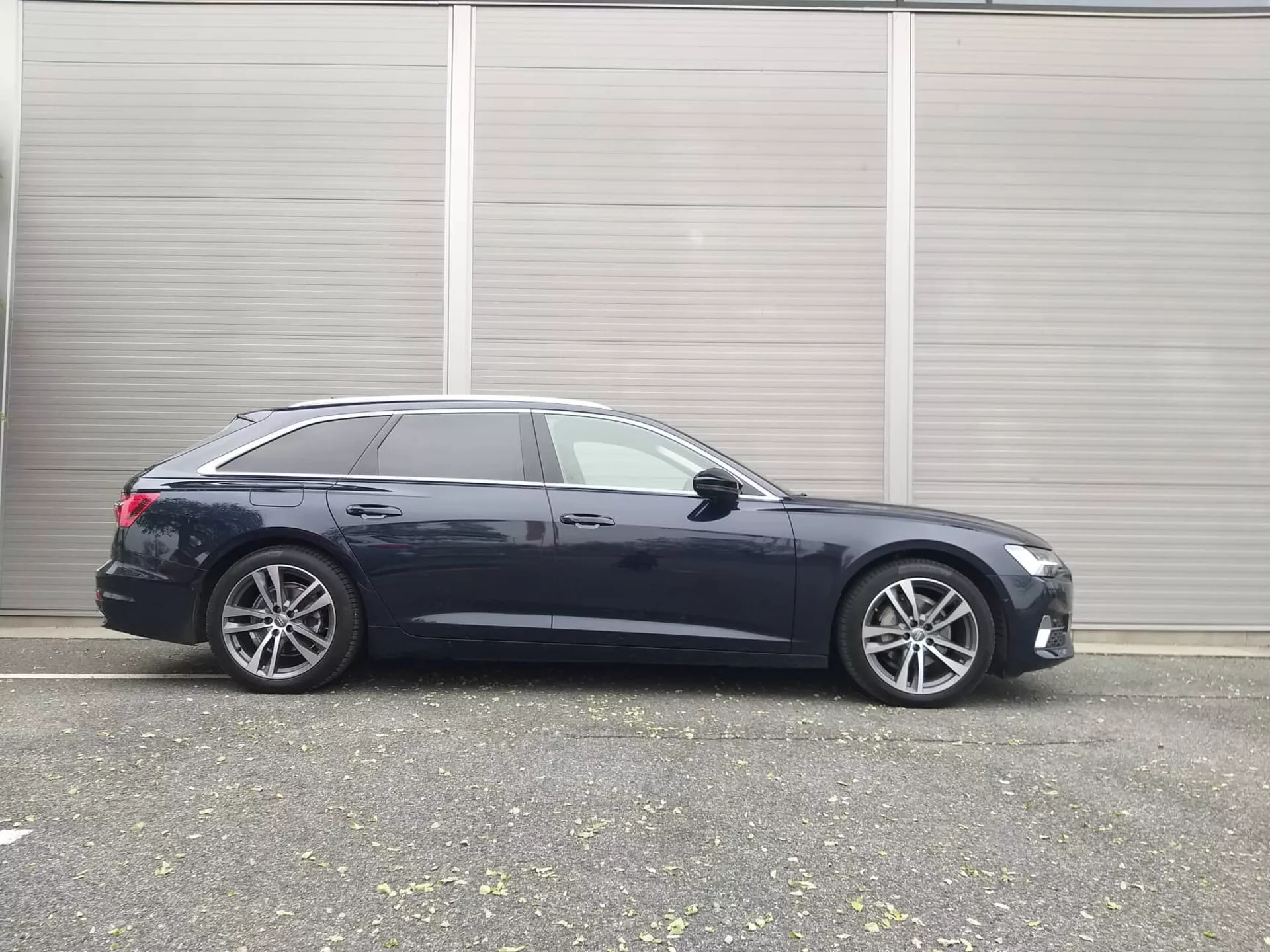 Boczny profil Audi A6 Kombi 2018, prezentujący elegancki design, zaawansowane funkcje technologiczne i premium felgi aluminiowe, zaparkowany w przemysłowym otoczeniu
