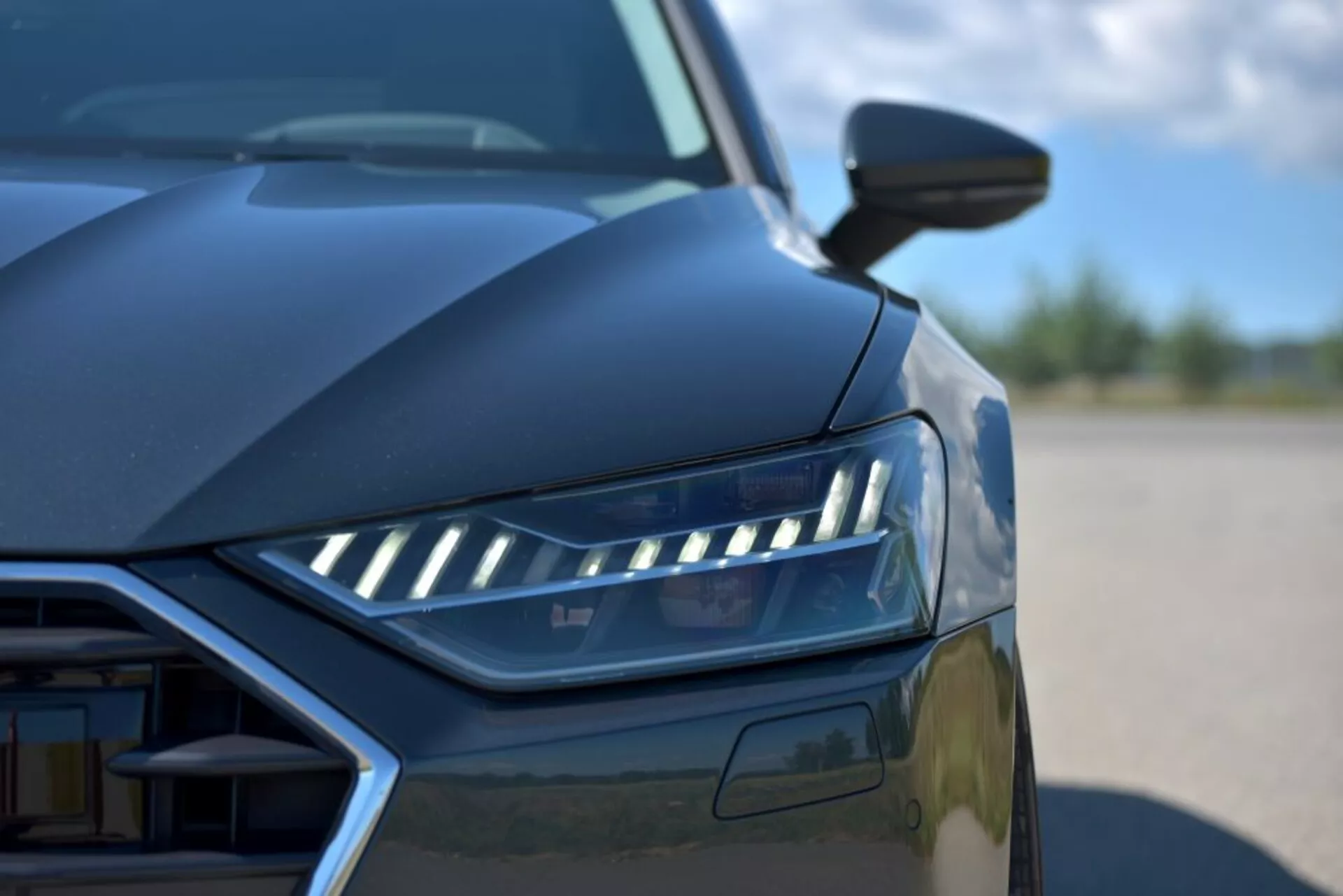 Zbliżenie Audi A7 Sportback 2018 ukazujące projekt LED-owych reflektorów, częściowy widok kratki i aerodynamiczne linie z niskiego kąta, prezentujące cechy nowoczesnego samochodu luksusowego i zaawansowaną technologię oświetleniową