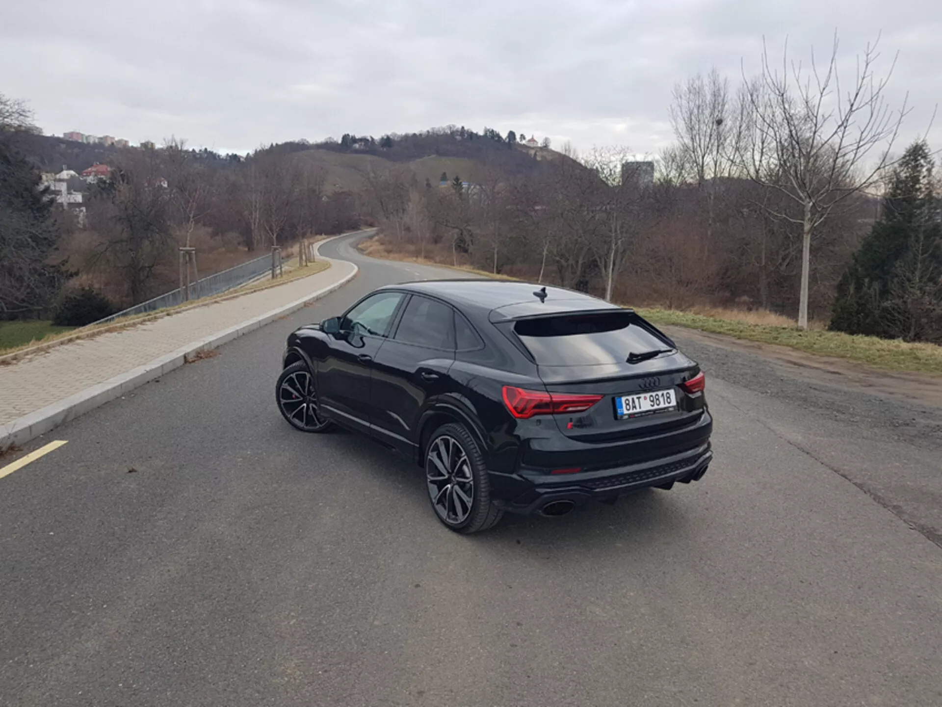 Audi Q3 RS z 2015 roku, ukośny tylny widok z trzech kwart na asfaltowej drodze, podkreślający eleganckie diody LED w światłach tylnych, wysokowydajny układ wydechowy i sportowe koła ze stopów