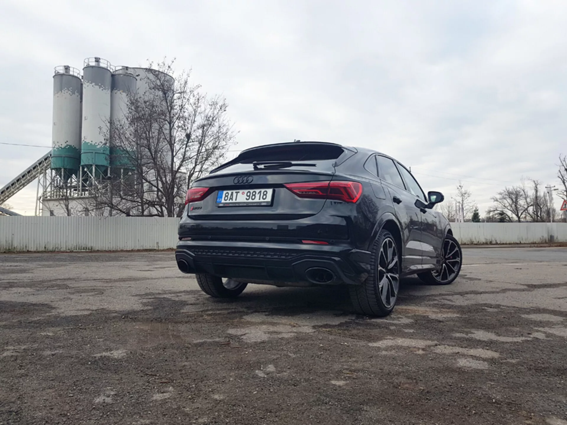 Audi Q3 RS 2015, nowoczesne SUV z widokiem z tyłu na trzy czwarte ukazującym sportowy design, duże felgi aluminiowe, podwójny układ wydechowy i przyciemniane szyby, zaparkowany w strefie przemysłowej.