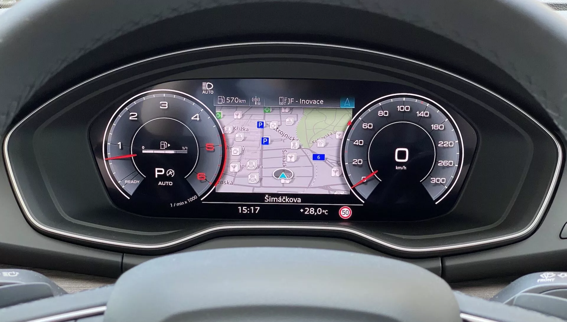 Widok z poziomu kierowcy na nowoczesny kokpit Audi Q5 Sportback 2020, ukazujący zestaw wskaźników z dwoma analogowymi tarczami i centralnym wyświetlaczem cyfrowym z mapą GPS, odczytem temperatury, zużyciem paliwa, wskaźnikami trybu jazdy oraz zegarem w wysokiej rozdzielczości na kolorowym interfejsie.