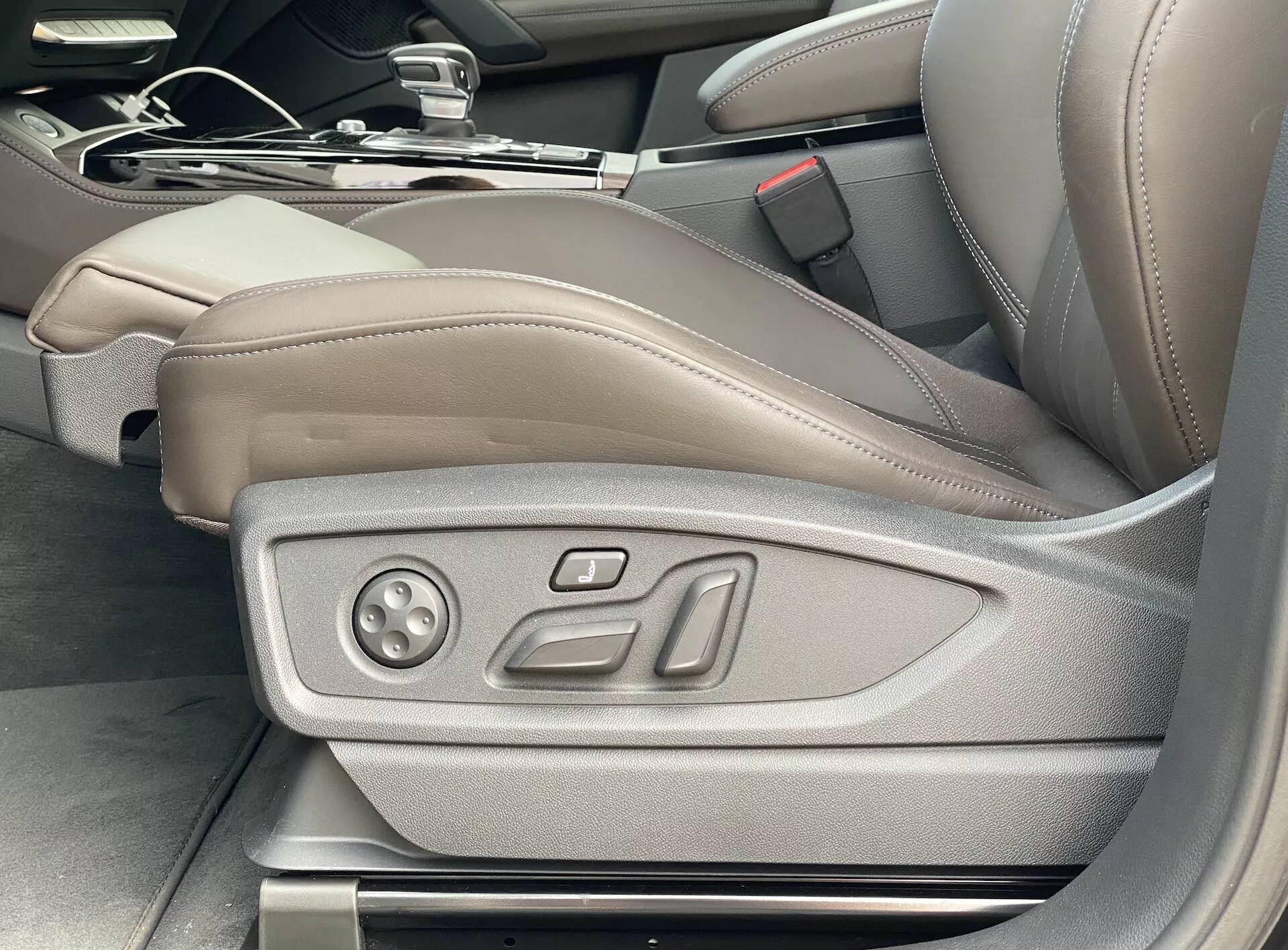 Widok wnętrza Audi Q5 2020 Sportback przedstawiający fotel kierowcy w jasnobrązowej/beżowej skórze z elektronicznymi elementami regulacji, podkreślający luksus i zaawansowaną technologię siedzisk, w tym potencjalne ustawienia pamięci; obraz zrobiony pod kątem z zewnątrz drzwi kierowcy.