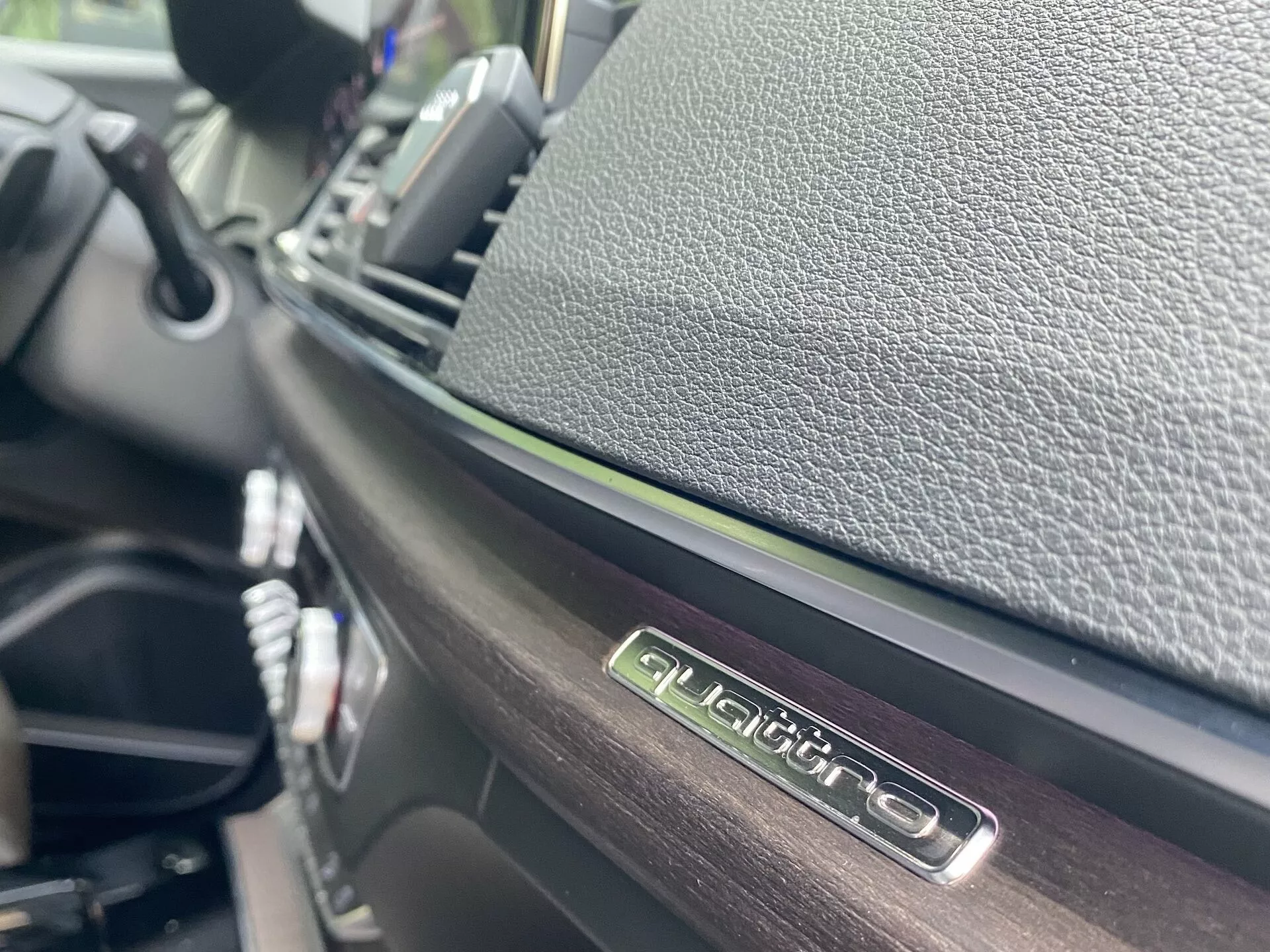 Zbliżenie wnętrza Audi Q5 2020 Sportback, koncentrujące się na emblemacie 'QUATTRO' na poziomie oczu, podkreślającym system napędu na cztery koła Audi. Z błyszczącym wykończeniem emblematów i kontrastującymi teksturowanymi materiałami, zdjęcie jest wykonane pod kątem z małą głębią ostrości, ukazując szczegóły deski rozdzielczej i centralnego panelu sterowania w rozmytym tle.