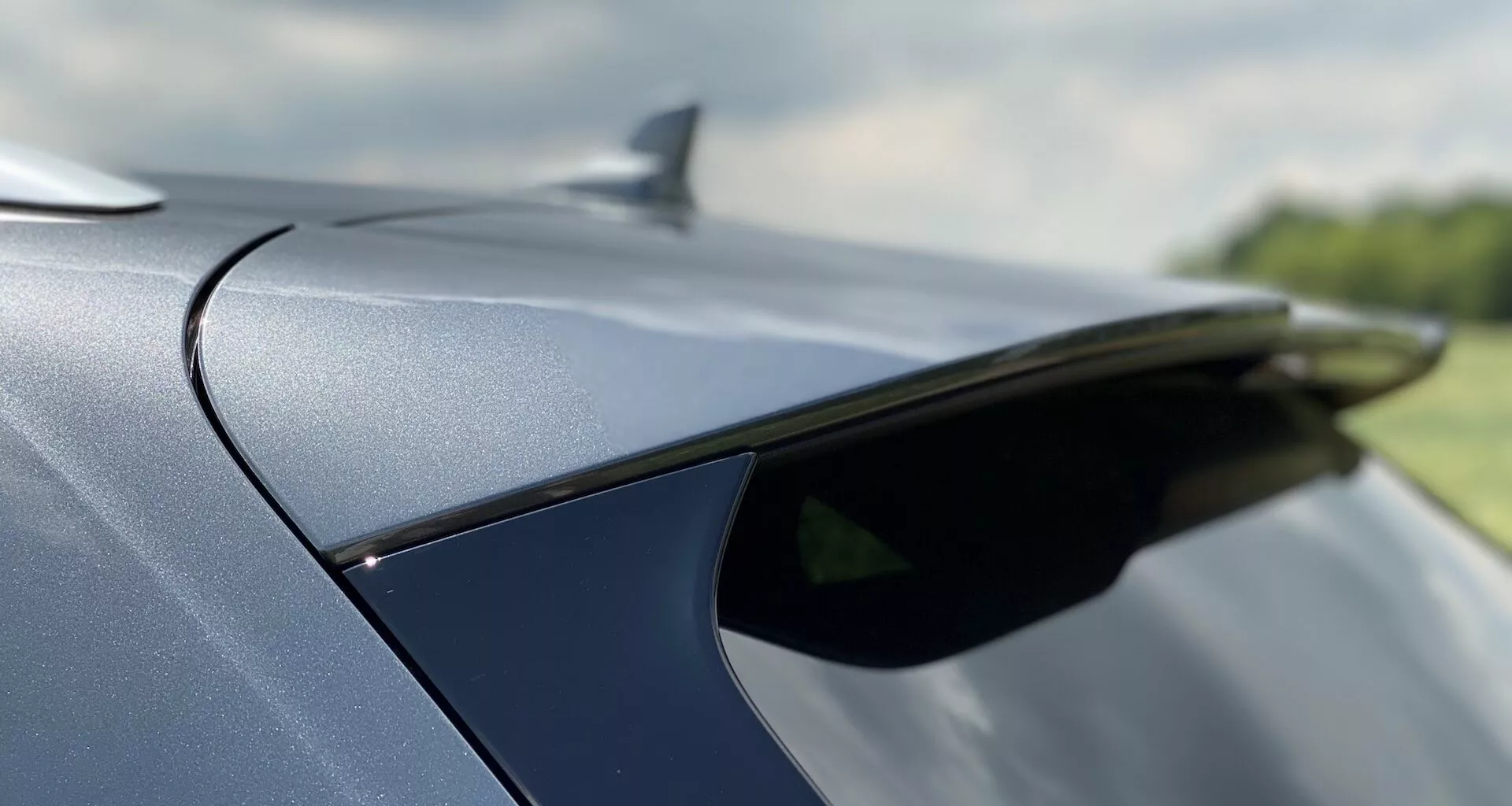 Zbliżenie tylnej części Audi Q5 2020 Sportback, podkreślające elegancki tylny spojler lub antenę w kształcie płetwy rekina oraz delikatnie opadającą linię dachu. Pojazd ma błyszczące, metaliczne wykończenie lakieru i wysokiej jakości detale materiałowe zewnętrzne. Mała głębia ostrości podkreśla elegancki design, a tło pozostaje rozmyte.