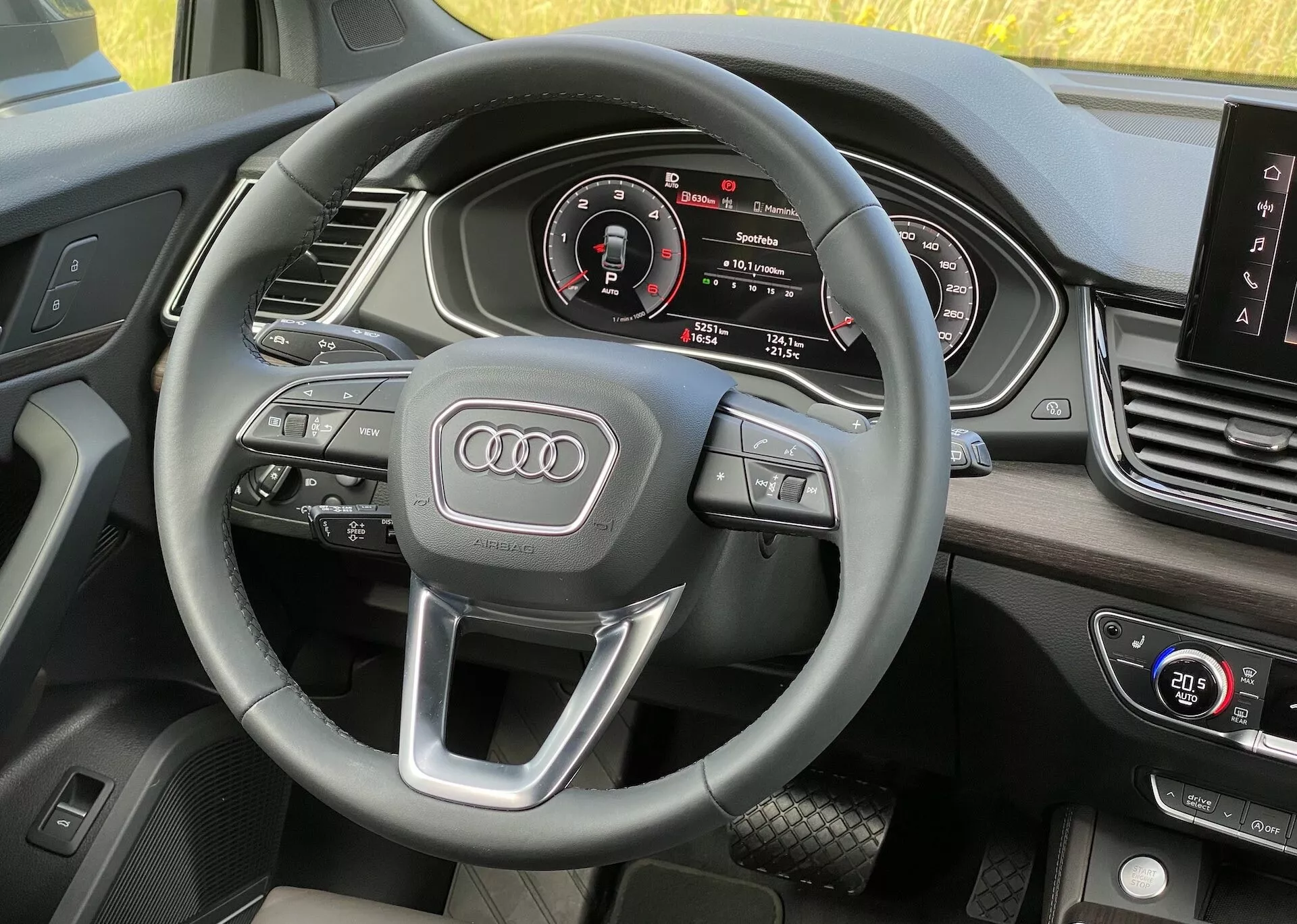 Wnętrze Audi Q5 Sportback 2020 z perspektywy kierowcy, pokazujące kierownicę z wielofunkcyjnymi przyciskami i emblematem Audi, cyfrową deską rozdzielczą z prędkościomierzem, obrotomierzem, centralnym wyświetlaczem informacyjno-rozrywkowym oraz sterowaniem klimatyzacją, z miękkimi, wysokiej jakości materiałami.
