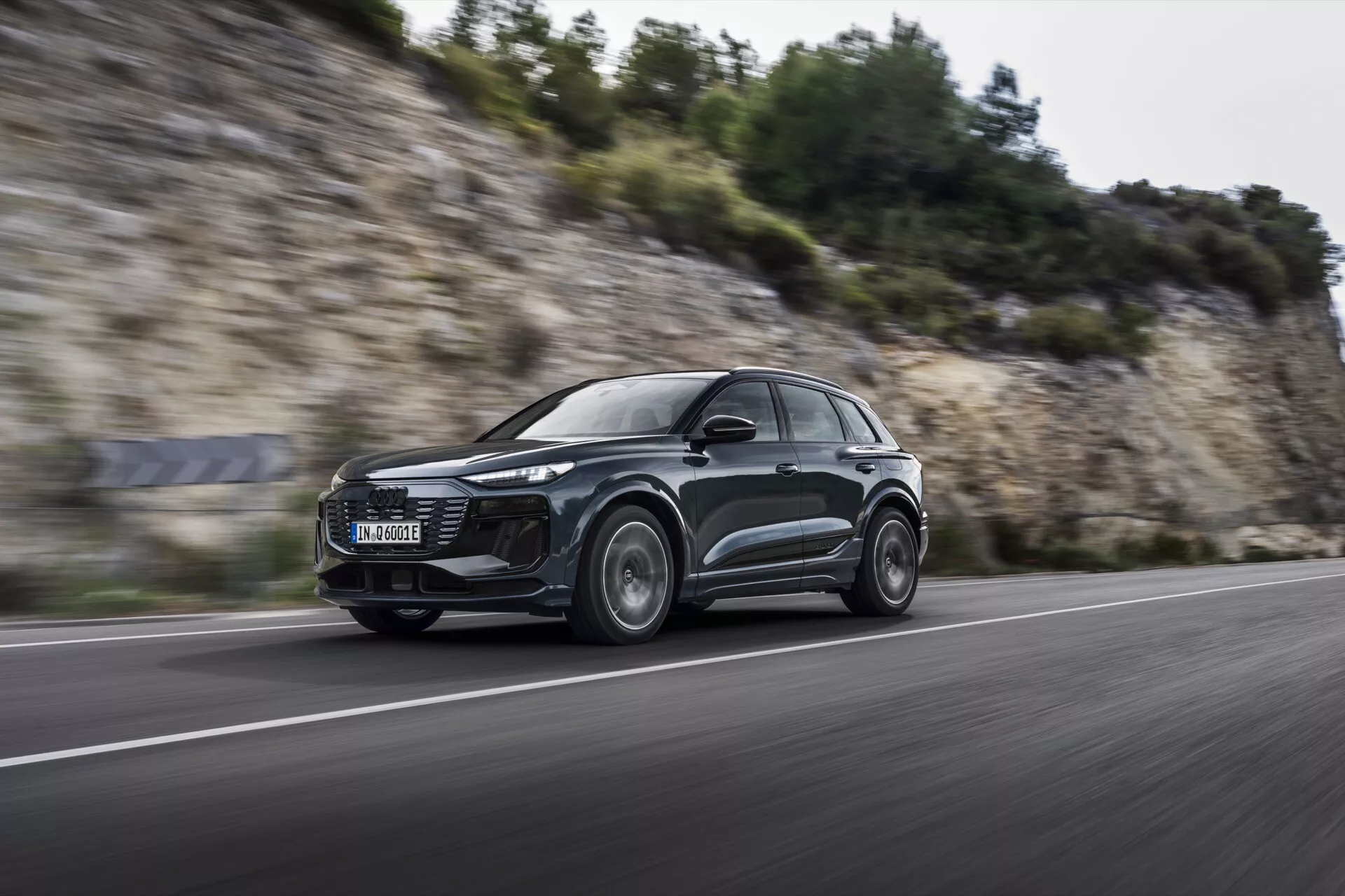 Dynamiczne ujęcie Audi Q6 e-tron 2024 w ruchu z niskiego, frontowego kąta, prezentujące jego smukły, aerodynamiczny design SUV, nowoczesne reflektory LED i koła aluminiowe z efektem rozmycia ruchu, sugerujące możliwości osiągów na asfaltowej drodze.