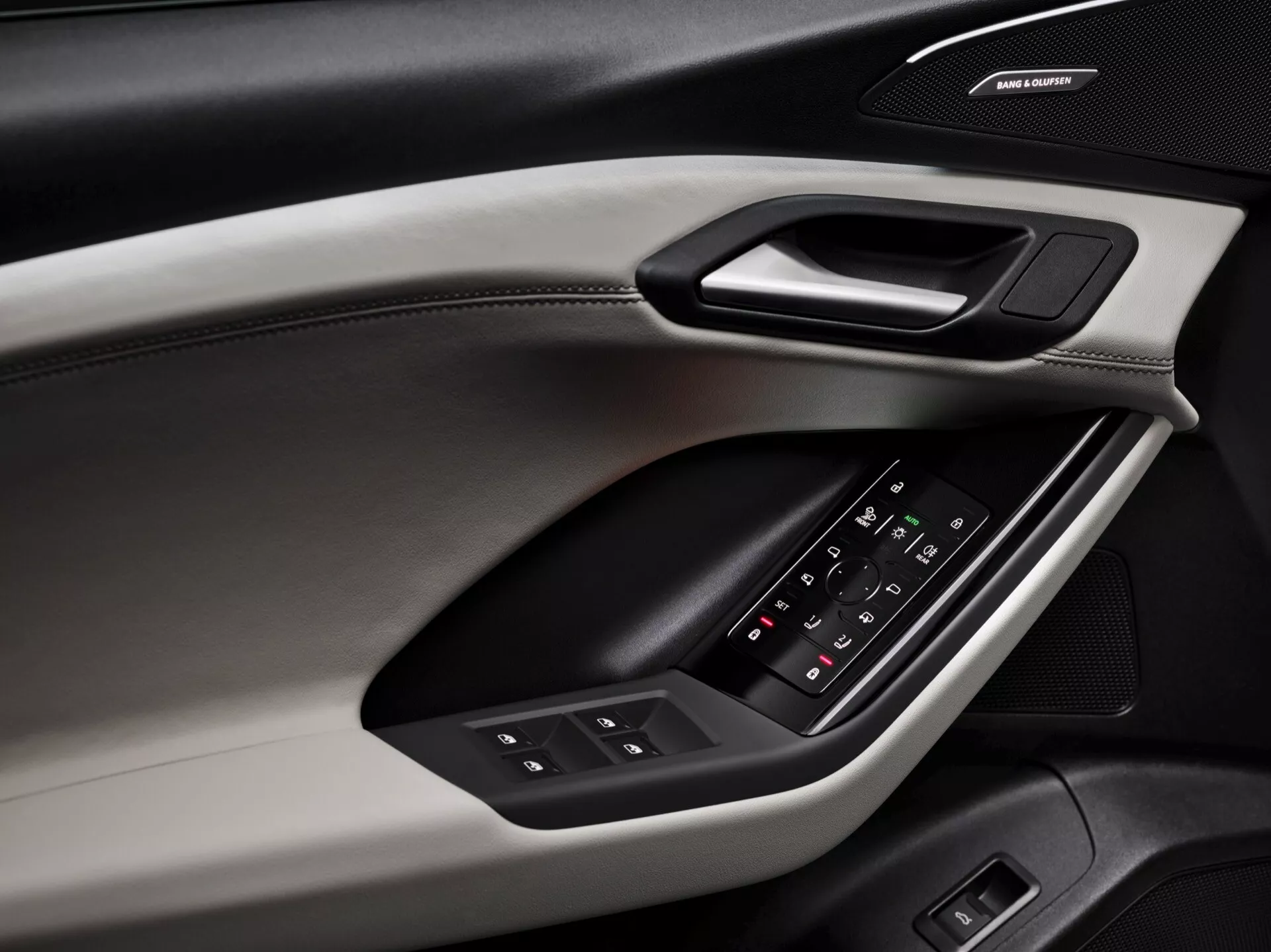 Zbliżenie na wewnętrzny panel drzwiowy Audi Q6 e-tron 2024, podkreślające elementy konstrukcyjne i funkcje. Panel drzwi, uchwycony pod kątem ukośnym, ujawnia różne materiały i tekstury, w tym górną część miękką w dotyku z widocznymi szwami, twardą osłonę mieszczącą ergonomiczną klamkę oraz wyściełany podłokietnik z podświetlanym panelem sterowania do okien i regulacji lusterek bocznych. Poniżej podłokietnika znajduje się system głośników ozdobiony markowym logo, co sugeruje obecność wysokiej jakości systemu audio. Schemat kolorów zawiera dwutonowy wzór, podkreślający walory estetyczne i funkcjonalne.