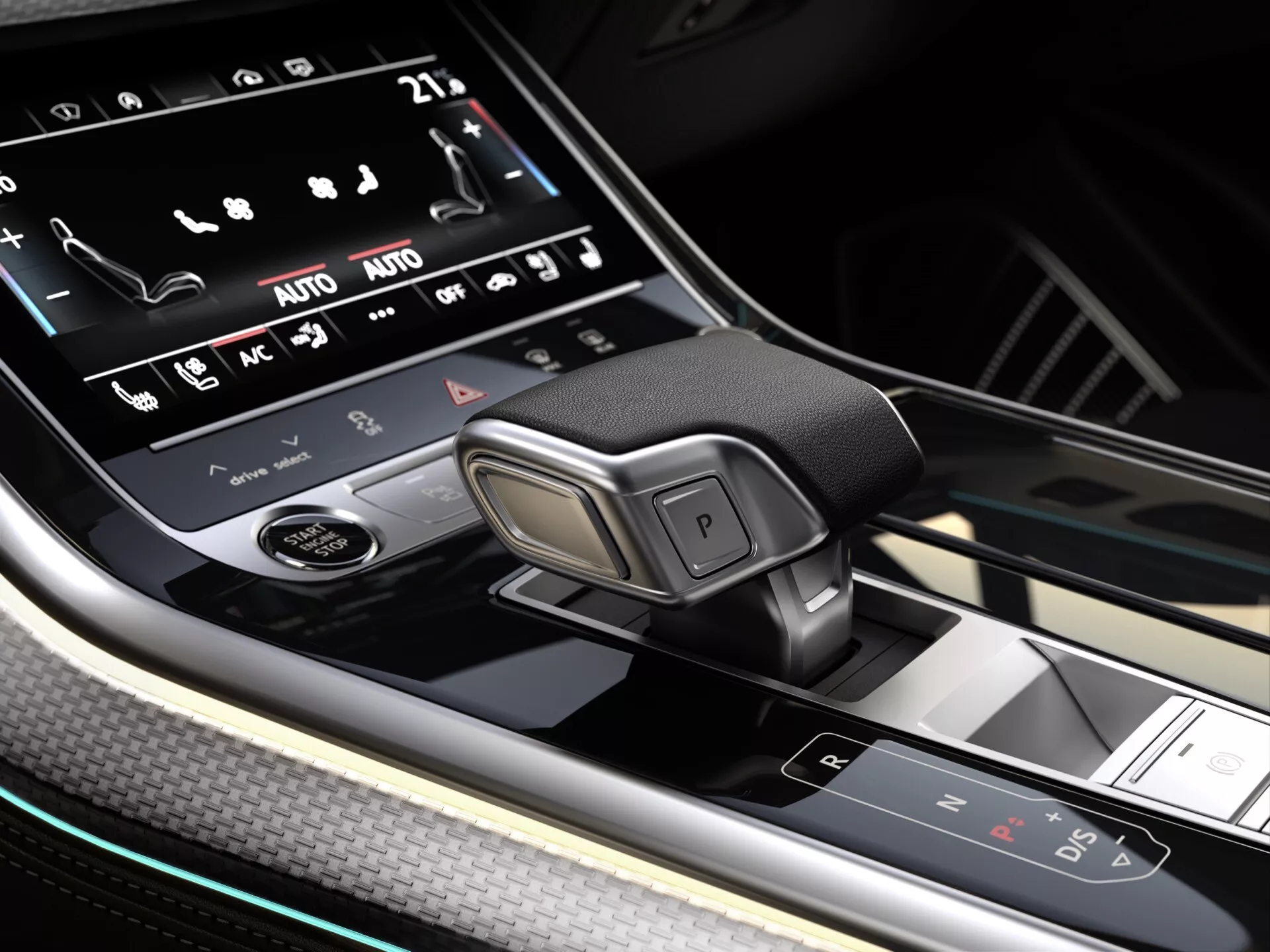 Zbliżenie na konsolę środkową Audi Q7 2024 (4M facelift 2), przedstawiające elektroniczny selektor biegów, system infotainment z ekranem dotykowym, i zaawansowane przyciski sterowania z akcentami z włókna węglowego i oświetleniem ambientowym