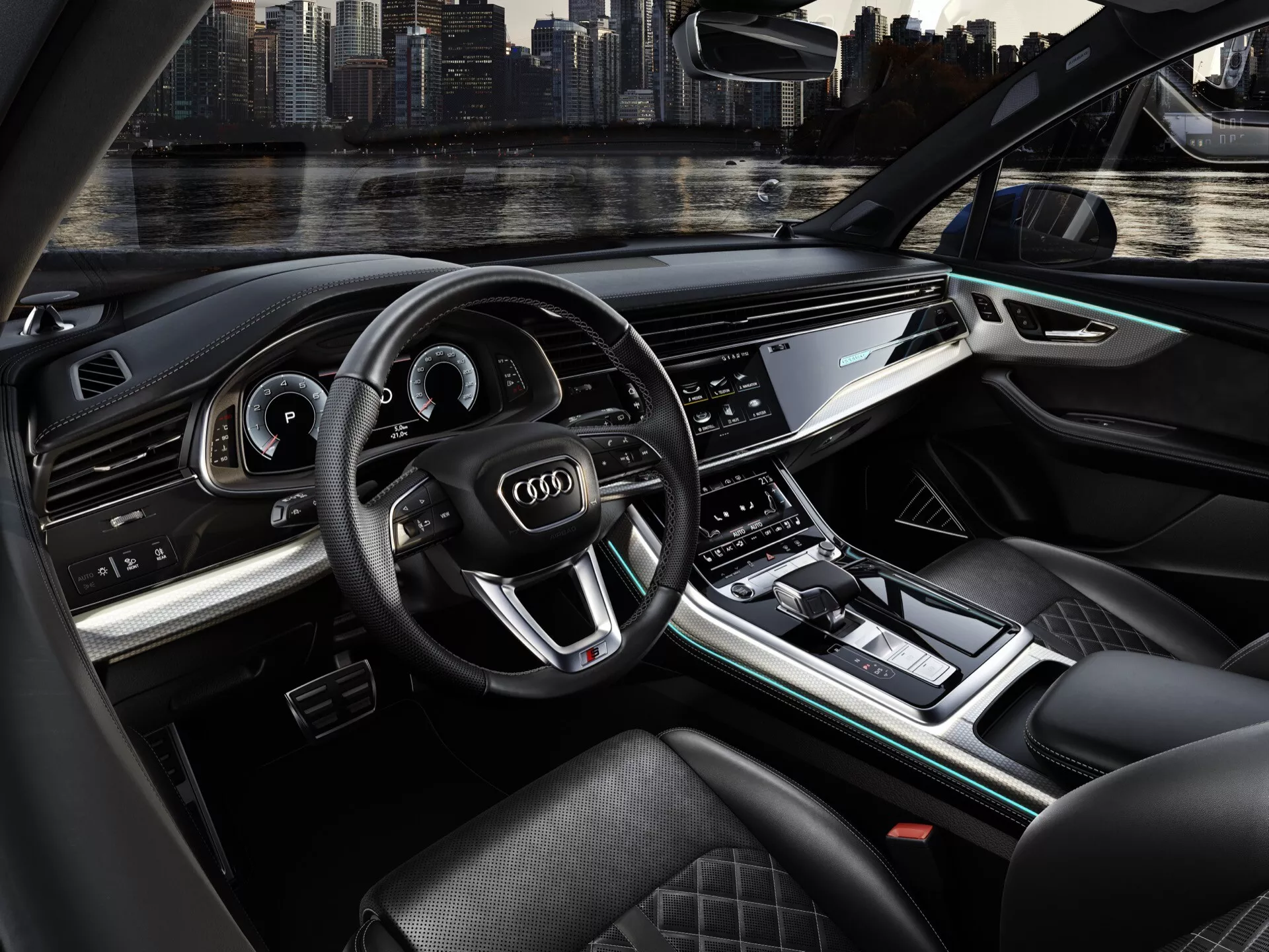 Widok wnętrza Audi Q7 2024 (4M-Facelift-2) z perspektywy kierowcy, podkreślający kierownicę, deske rozdzielczą, konsolę środkową i materiały premium z oświetleniem ambientowym