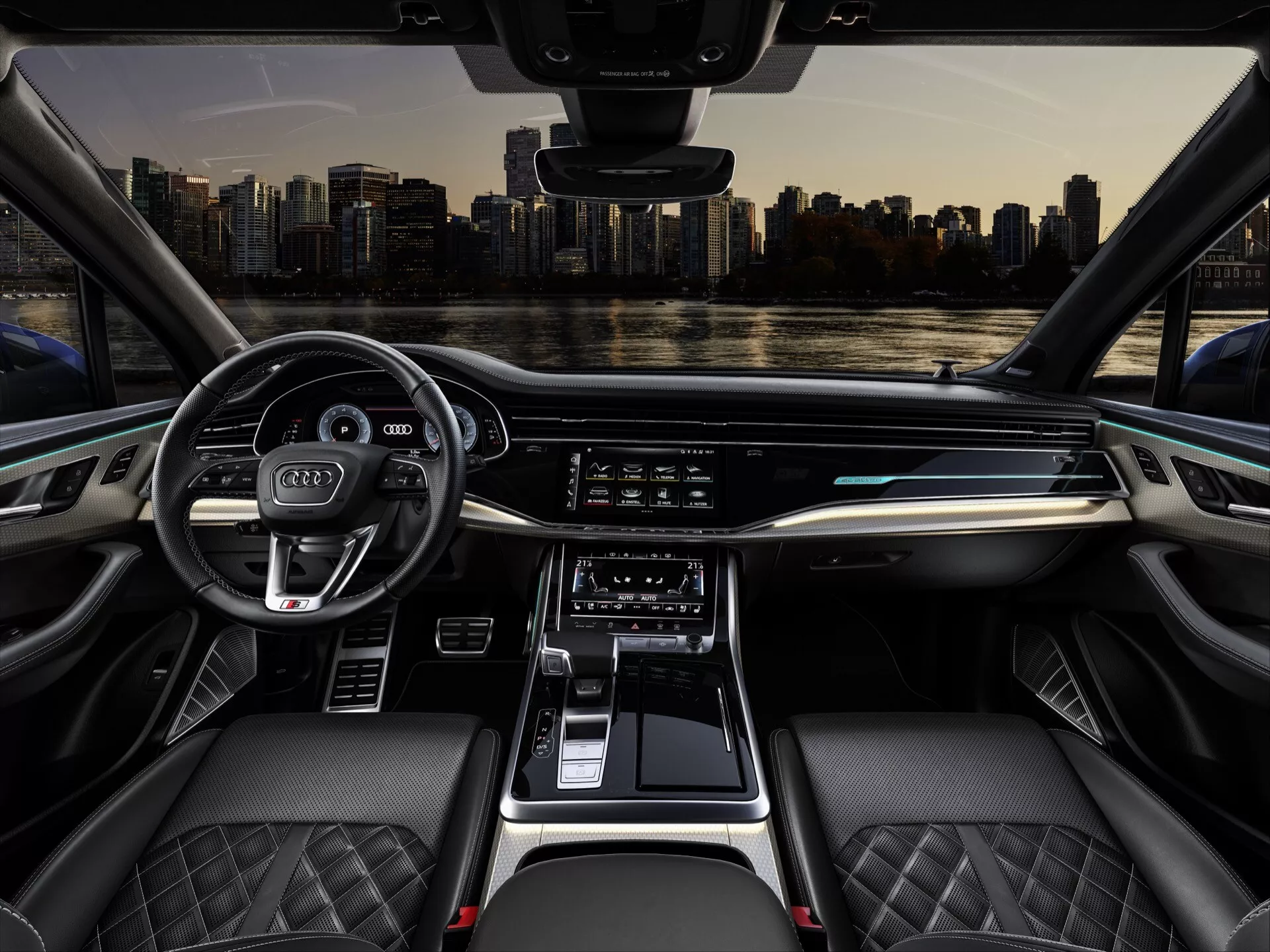 Widok wewnętrzny kokpitu Audi Q7 2024 (4M-Facelift-2) z perspektywy środkowego tylnej siedzenia, przedstawiający przednią deskę rozdzielczą wyposażoną w nowoczesną technologię, w tym szeroki wyświetlacz cyfrowy do nawigacji i mediów, elegancki panel kontroli klimatyzacji, ergonomiczną dźwignię zmiany biegów i luksusowe skórzane siedzenia z pikowanym szwem.