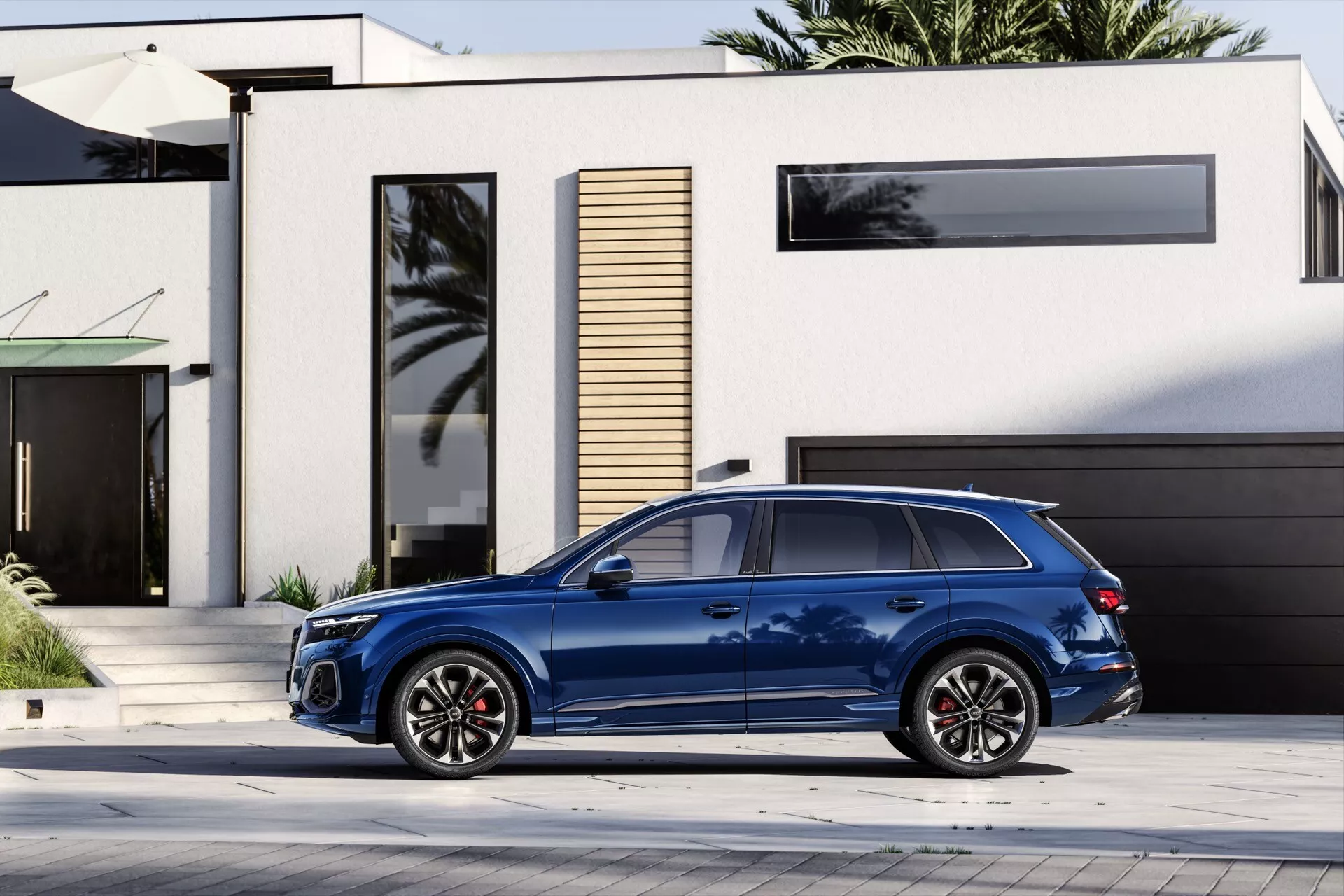 Boczny widok niebieskiego SUV-a Audi Q7 4M facelift 2024 zaparkowanego na podjeździe przy nowoczesnym domu, z pięcioramiennymi felgami aluminiowymi z czerwonymi zaciskami hamulcowymi, widocznym systemem relingów dachowych do transportu bagażu, przyciemnianymi szybami zapewniającymi prywatność oraz eleganckim designem sugerującym nowoczesne technologie motoryzacyjne.