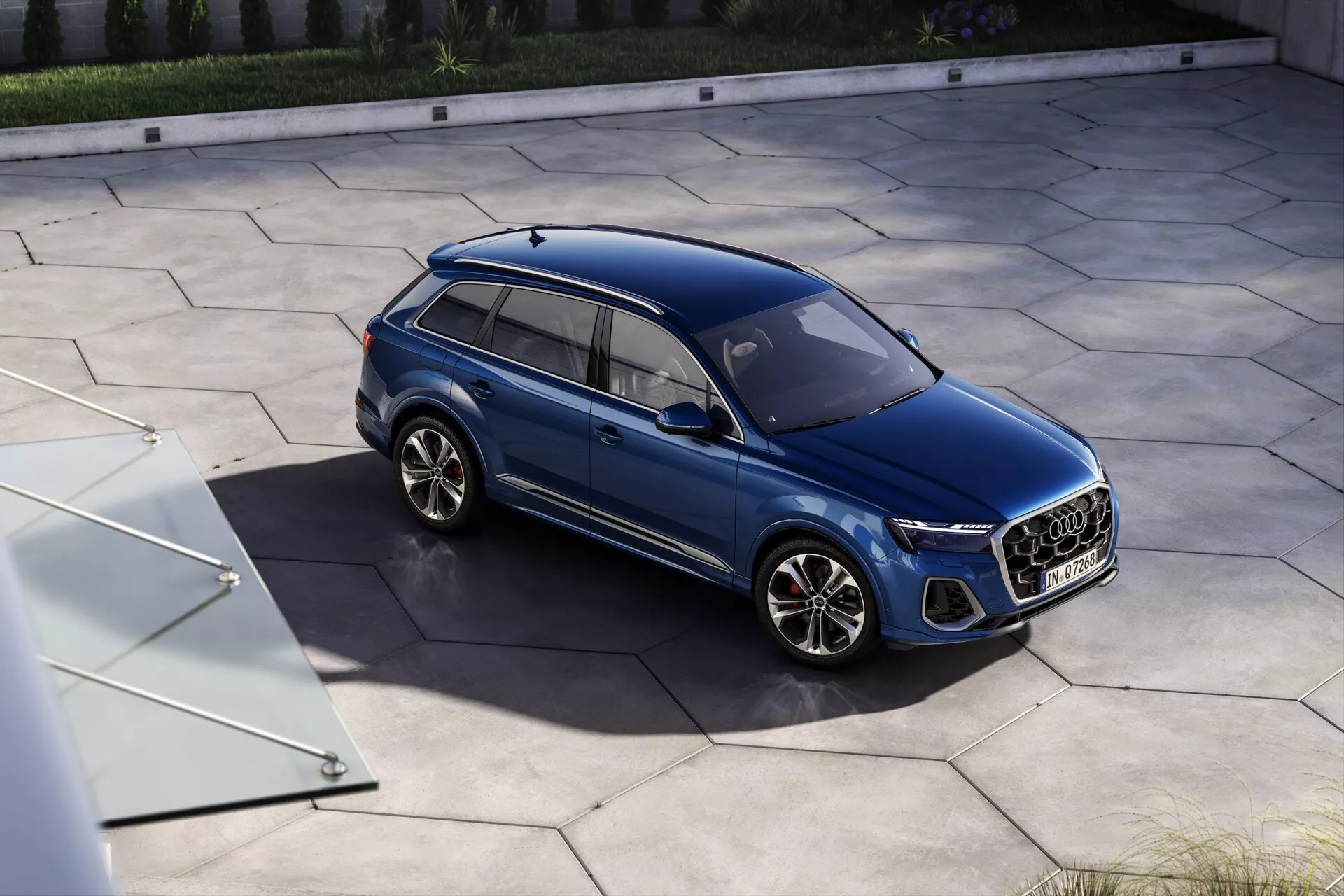SUV Audi Q7 2024 w kolorze niebieskim, widok z wysokiego kąta ukazujący grill przedni, reflektory LED i sportowe felgi aluminiowe w luksusowym otoczeniu mieszkalnym