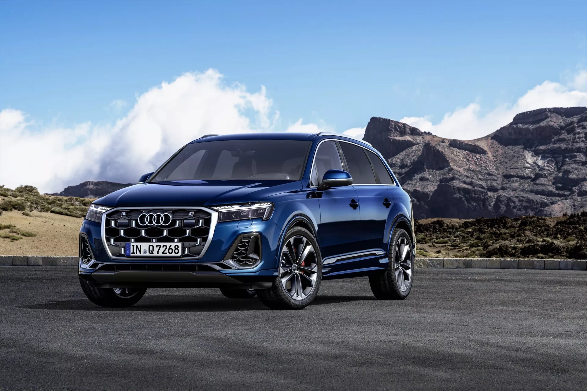 Niebieskie Audi Q7 2024 (4M Facelift 2) z LEDowymi reflektorami, przednią kratą z logo, felgami aluminiowymi o wieloramiennej konstrukcji i aerodynamicznym profilem bocznym na tle górskiego krajobrazu pod czystym niebem