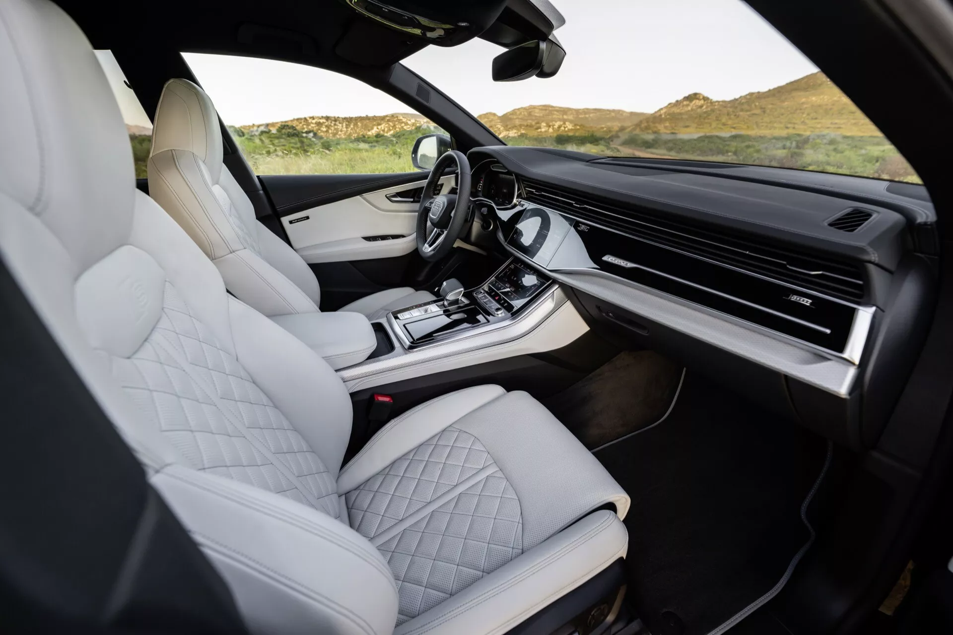 Wnętrze Audi Q8 2023 (4M-Facelift) prezentujące białe siedzenia z pikowaną skórą, luksusowy design konsoli środkowej, rozbudowany system infotainment z ekranem dotykowym i nowoczesne, ergonomiczne funkcje, zdjęcie z perspektywy pasażera