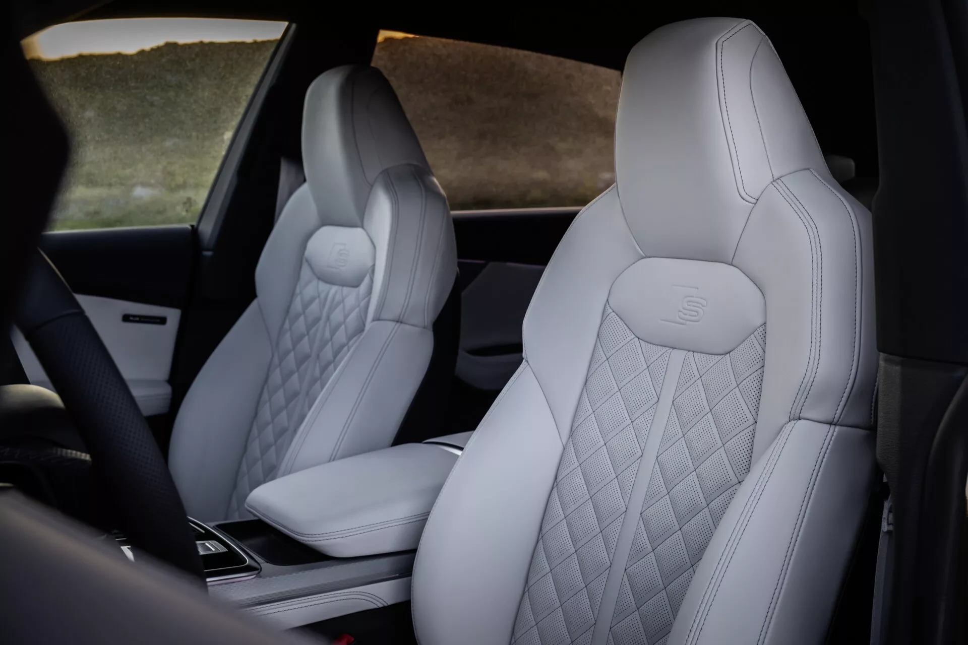 Widok wnętrza Audi Q8 2023 (4M-Facelift) podkreślający luksusowe przednie siedzenia z jasną, pikowaną tapicerką i wytłoczonym logo Mercedes-Benz, z widokiem na zaawansowaną technologicznie konsolę środkową z perspektywy tylnej i z boku.
