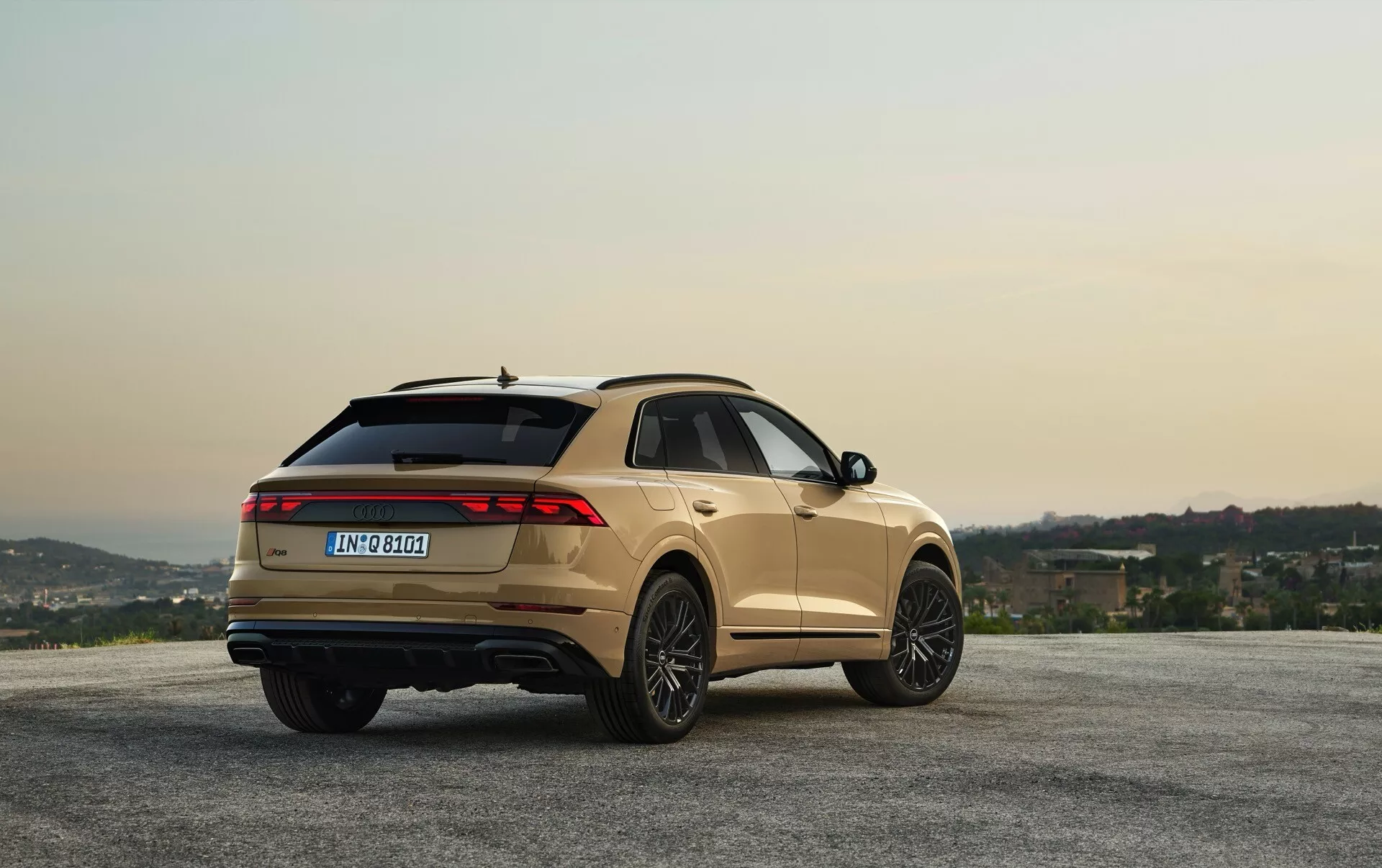 Audi Q8 2023 (4M-Facelift) w metalicznym wykończeniu zaparkowane na punkcie widokowym z wzgórzami i niebem o świcie/zmierzchu, pokazujące kąt z tyłu trzy czwarte do przeglądu designu i funkcji