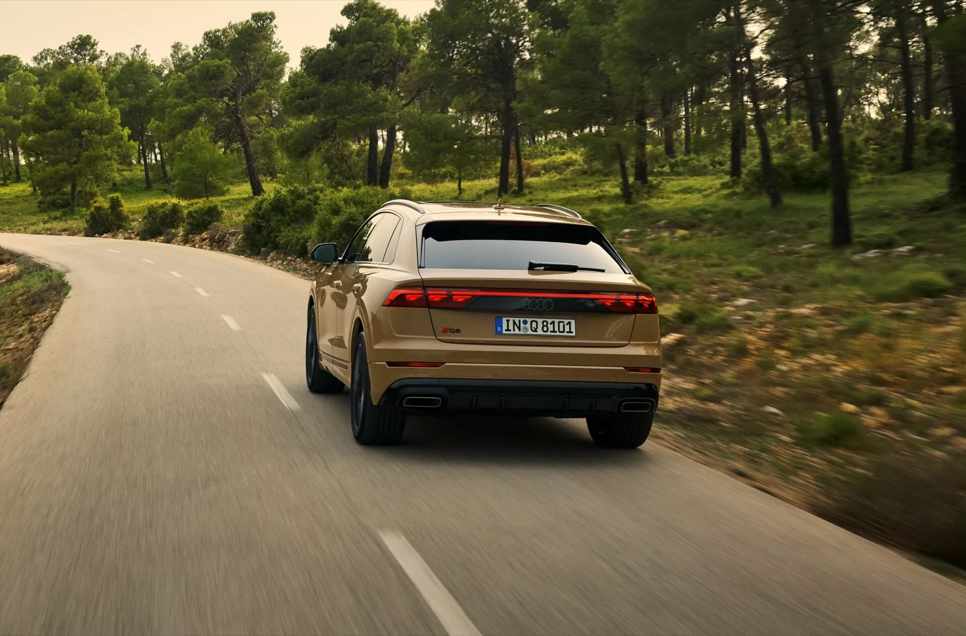 Tylny widok Audi Q8 2023 (4M-Facelift) jadącego krętą drogą przez las, pokazujący prawy tylny kwadrant z LEDowymi światłami tylnymi, podwójnym wydechem i nowoczesnymi cechami wzornictwa