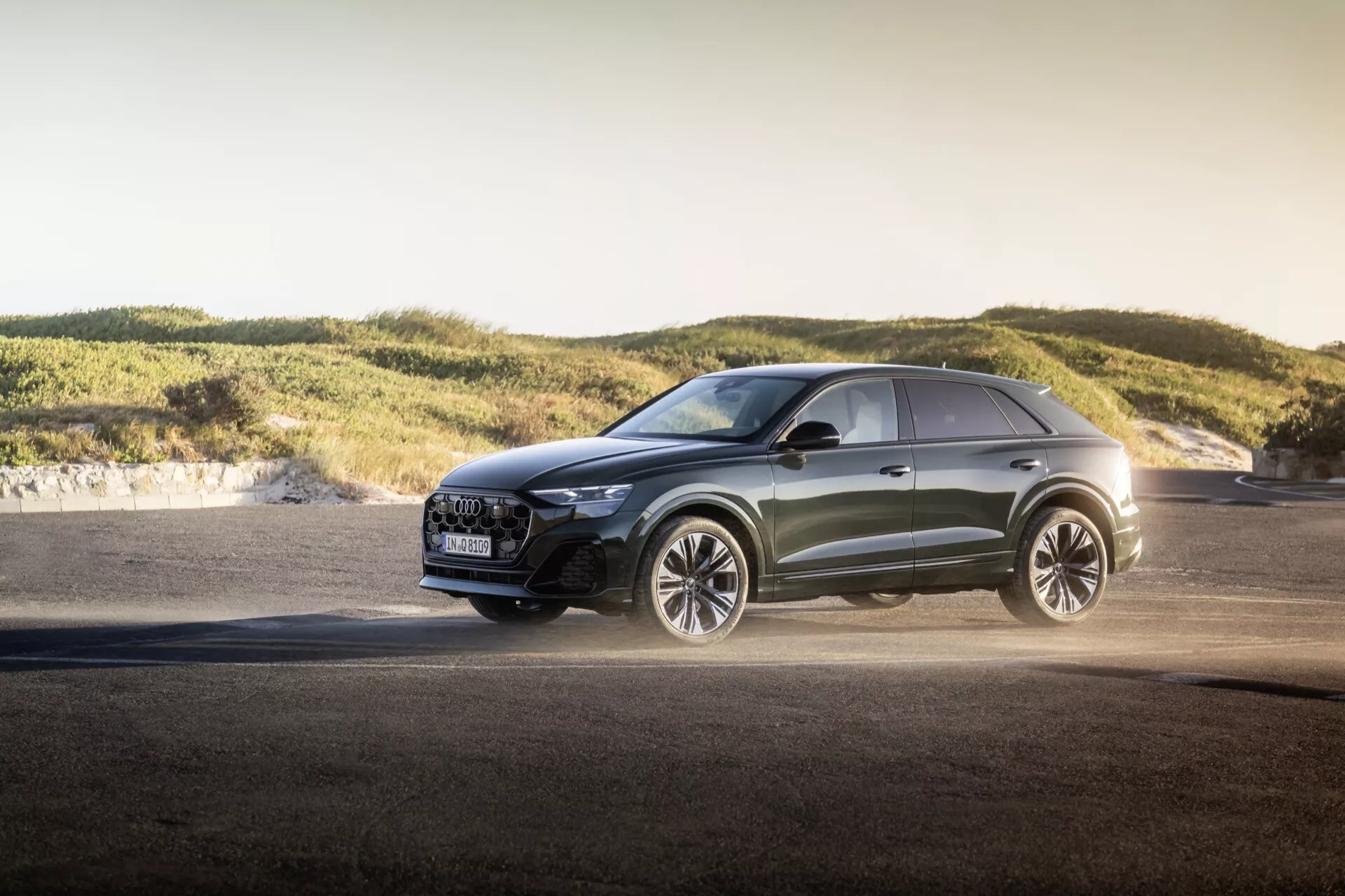 Nowoczesny crossover Audi Q8 2023 (4M-Facelift) na zewnątrz podczas złotej godziny, prezentujący zaawansowane reflektory LED, luksusową kratę z funkcjami bezpieczeństwa, duże koła ze stopów lekkich skoncentrowane na wydajności, metaliczny lakier i sportowe linie projektowe na tle asfaltu i łagodnych wzgórz, podkreślający wszechstronne możliwości i design