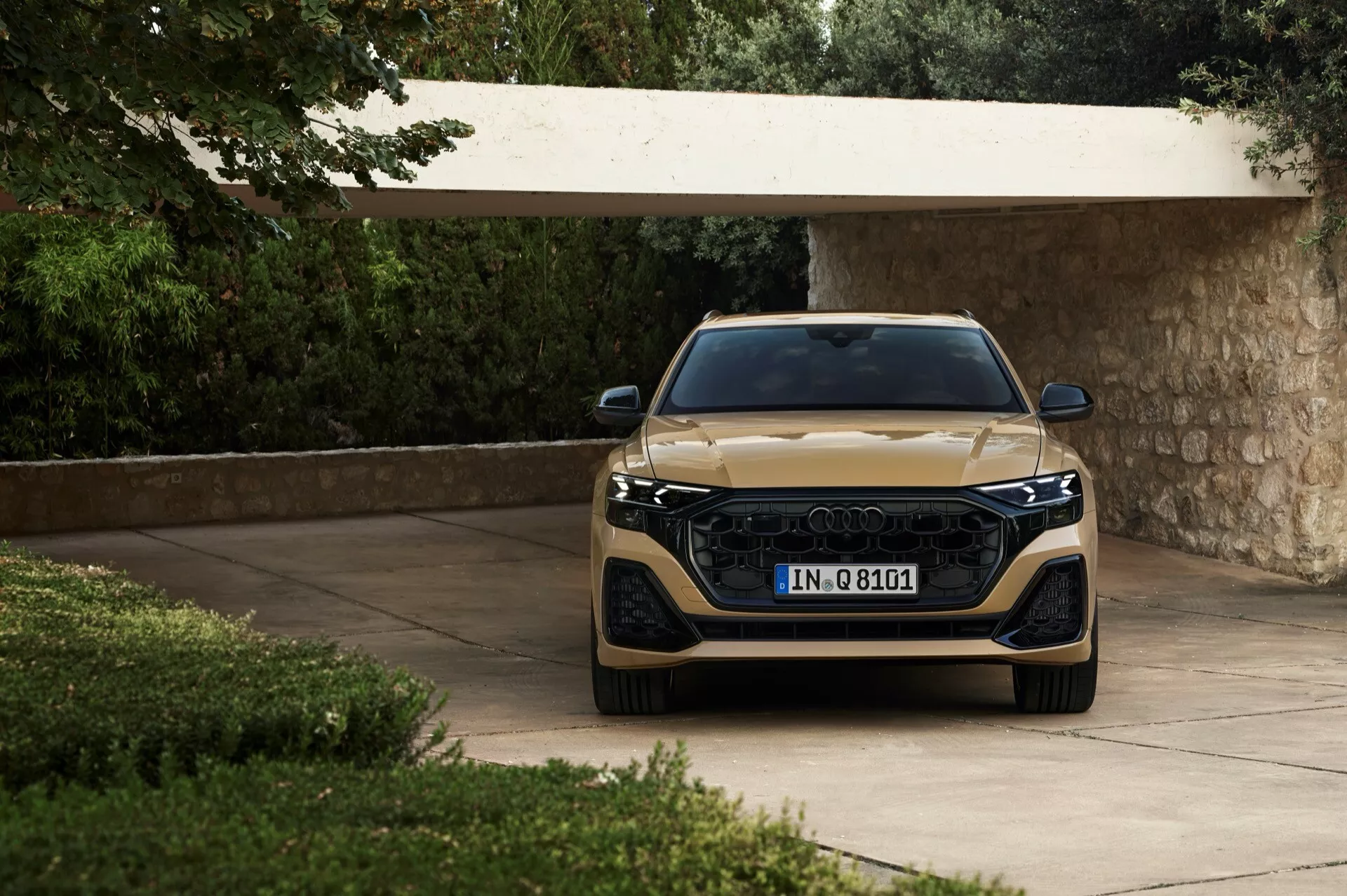 Audi Q8 2023 (4M-facelift) pokazane z frontowego kąta, podkreślające jego szeroką grillę, eleganckie reflektory LED i metaliczne wykończenie, umieszczone na podjeździe otoczonym bujną zielenią