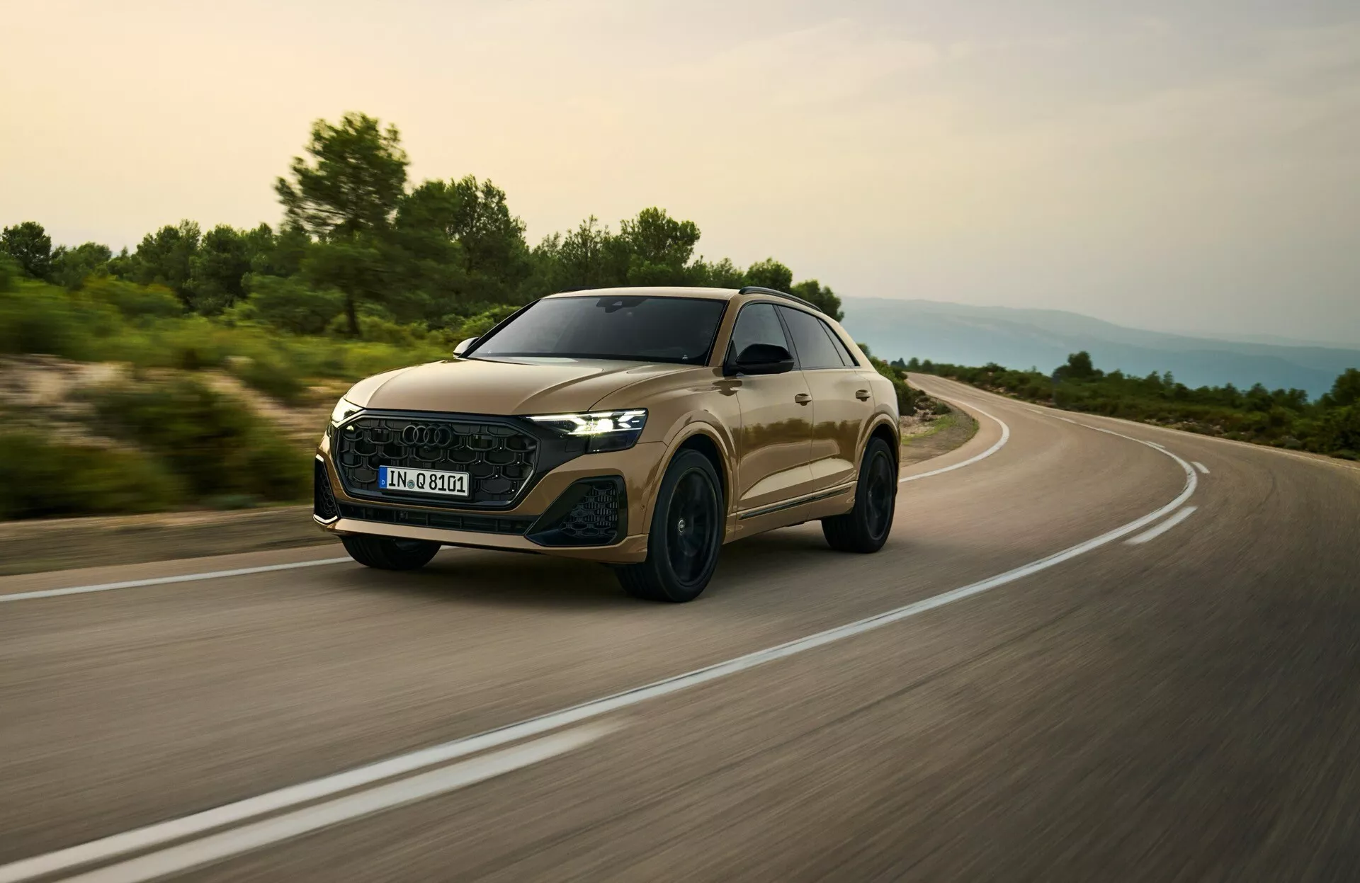 Audi Q8 2023 (model 4M facelift) uchwycone w dynamicznej scenie jazdy, skupiające się na jego aerodynamicznym grillu, reflektorach LED i smukłym profilu z niskiego kąta przednich trzech czwartych sugerującym prędkość i cechy premium