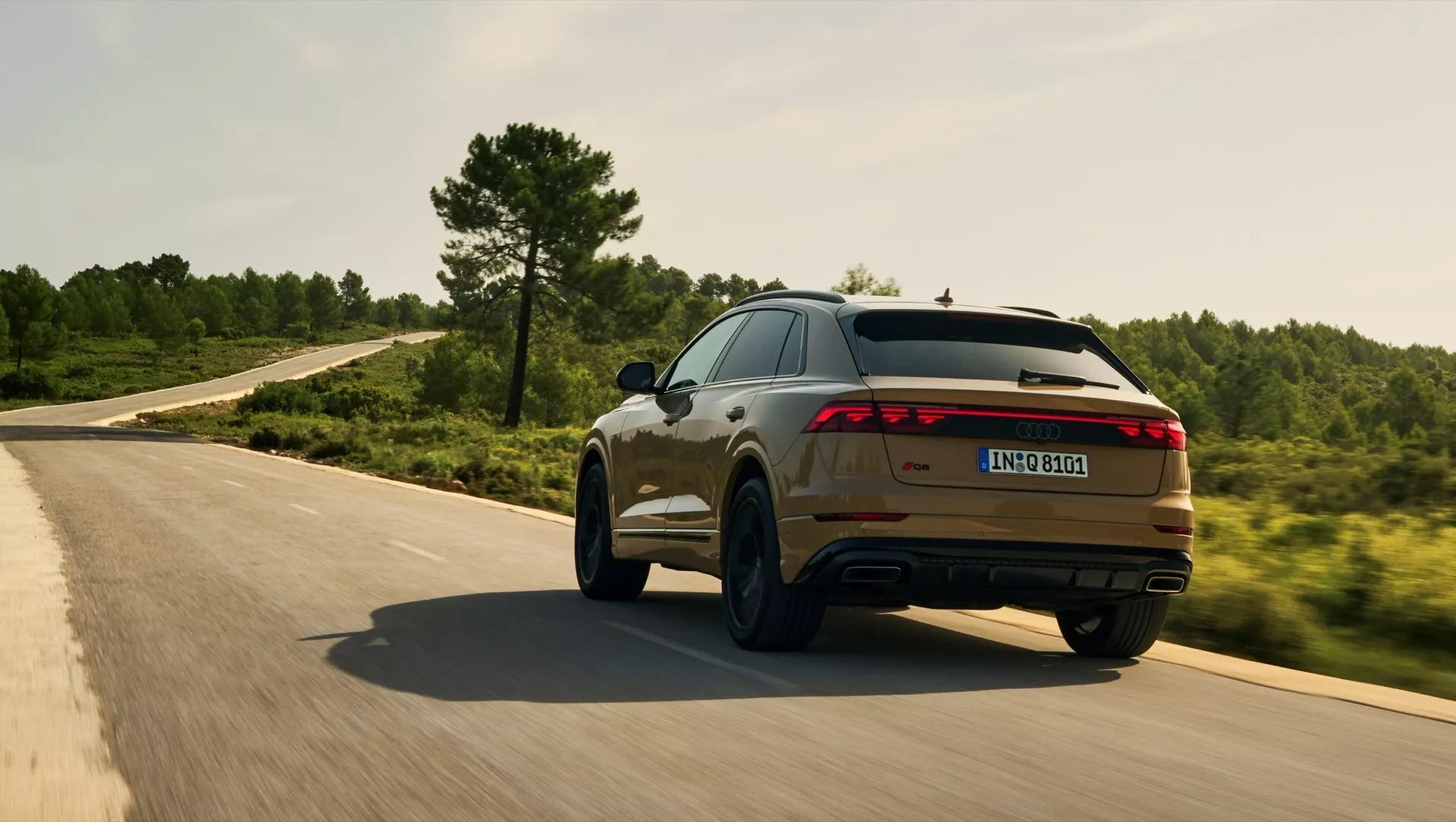 Audi Q8 2023 (4M-Facelift) w ruchu na zakręconej drodze, pokazujące swój sportowy tylny i boczny profil z belką LED, podwójnym wydechem i metalicznym wykończeniem