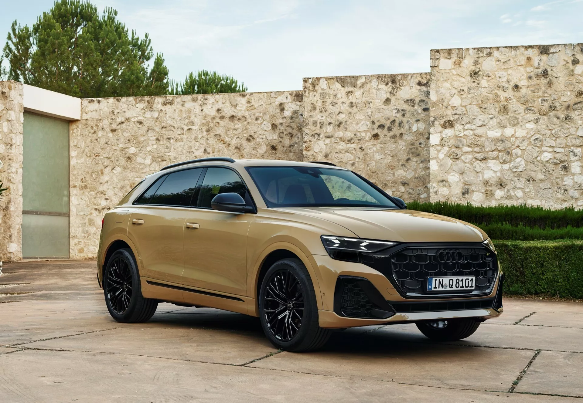 Trzy czwarte widoku z przodu Audi Q8 2023 (4M-facelift) w złotym odcieniu, prezentujący jego aerodynamiczny profil boczny, charakterystyczną atrapę, reflektory LED i luksusowe koła ze stopu, zaparkowane z lekkim skrętem w stronę kamery na eleganckim tle
