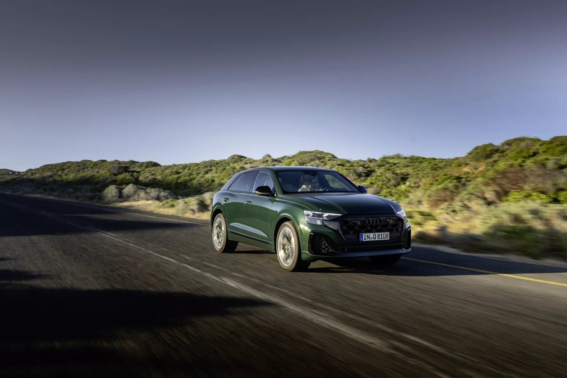 Audi Q8 2023 (4M-Facelift) w ruchu, prezentujące aerodynamiczny kształt, ostre światła LED, dużą atrapę z zaawansowanym chłodzeniem, sportowe alufelgi i funkcje wysokiej wydajności z przedniego trzykwartalnego kąta na autostradzie