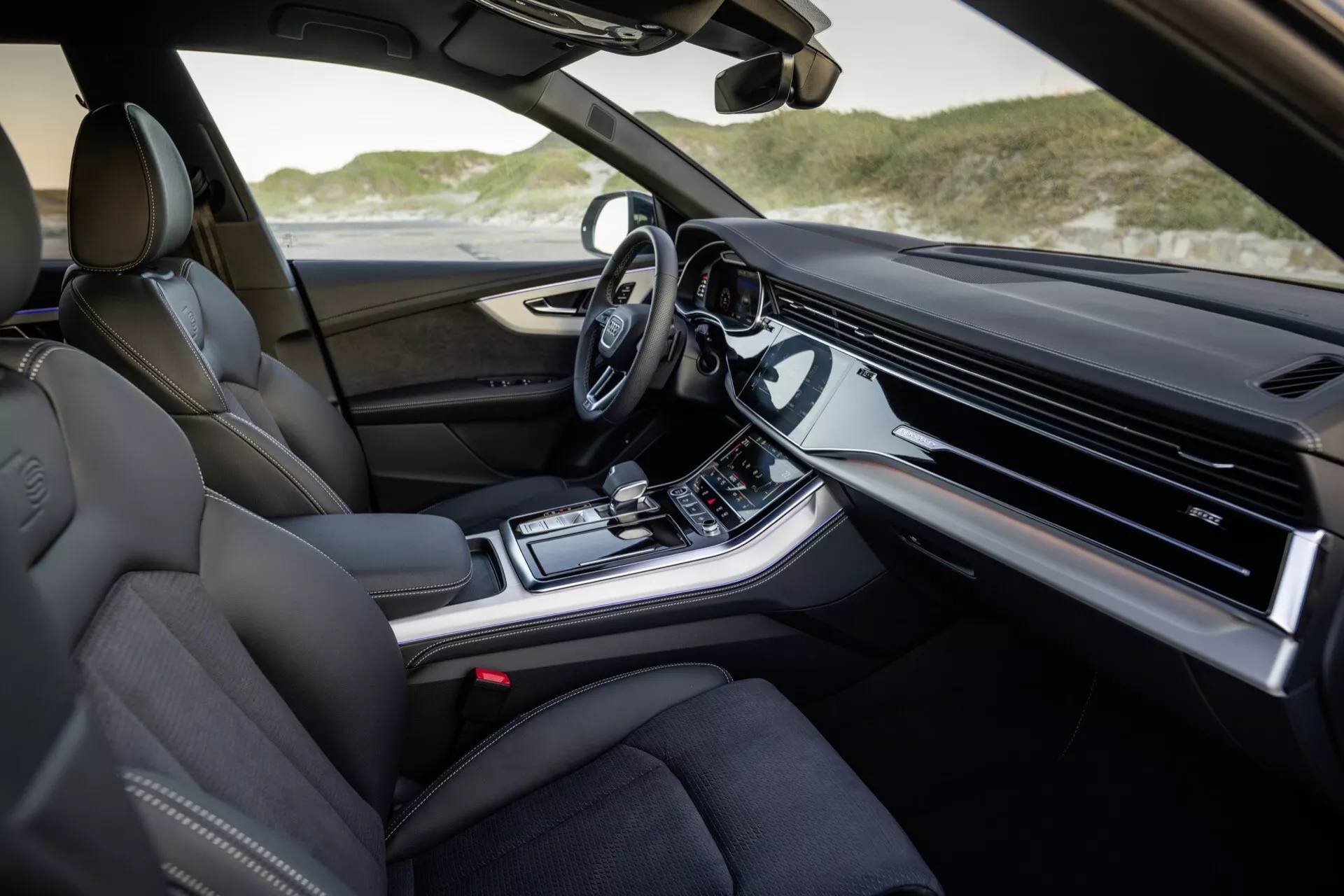 Widok wnętrza Audi Q8 2023 (4M-Facelift) od strony pasażera z luksusowymi skórzanymi siedzeniami, zaawansowanym deskiem rozdzielczym z zintegrowanym wyświetlaczem infotainment, konsolą środkową z kontrolami klimatyzacji i trybem jazdy, nowoczesną automatyczną dźwignią zmiany biegów i kierownicą wyposażoną w technologie