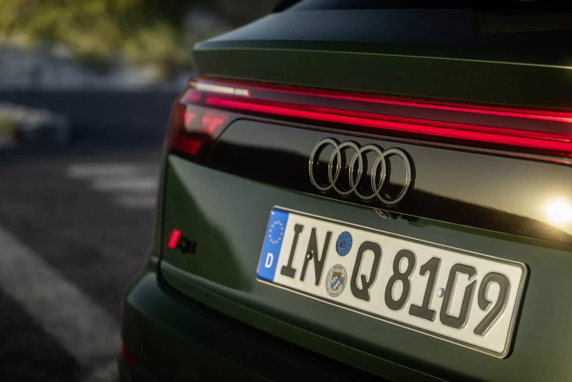 Zbliżony tylny widok zielonego Audi Q8 z 2023 roku po liftingu 4M, pokazujący odznakę Audi, poziomy pasek LED, europejską tablicę rejestracyjną z Ingolstadt, sportowy spojler oraz szczegółowo zaprojektowaną pokrywę bagażnika z polerowanym metalicznym wykończeniem.