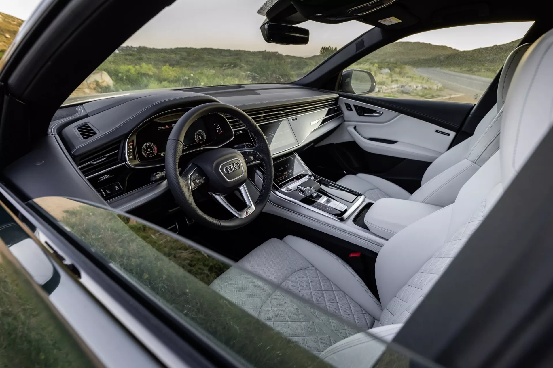 Widok wnętrza Audi Q8 2023 (4M-Facelift) podkreślający kokpit po stronie kierowcy z cyfrowym zegarem, systemem informacyjno-rozrywkowym dotykowym i luksusowymi wykończeniami, takimi jak tapicerka skórzana i metalowe akcenty