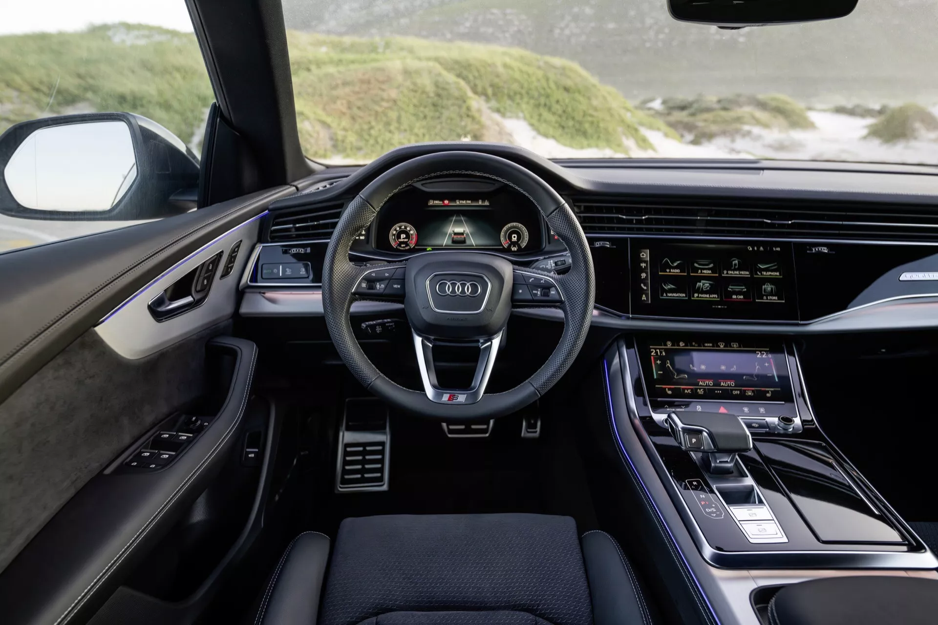 Widok wnętrza Audi Q8 2023 (4M-Facelift) z perspektywy kierowcy podkreślający nowoczesny deska rozdzielcza, trójramienne kierownica z przyciskami sterującymi, podwójne wyświetlacze cyfrowe dla zegarów i systemu informacyjno-rozrywkowego, oraz luksusowe akcenty dizajnerskie.