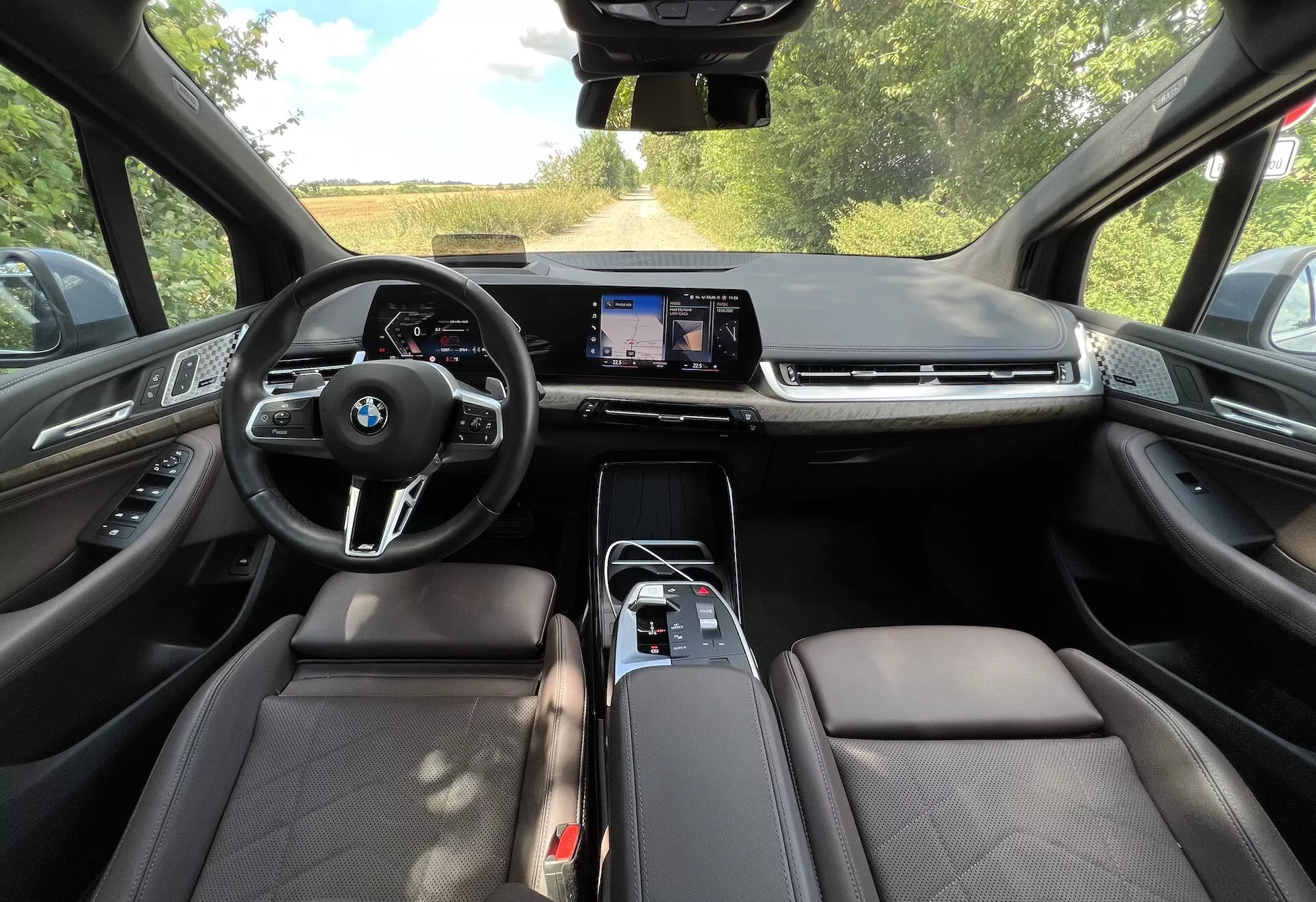 Wnętrze BMW Serii 2 Active Gran Tourer 2022 z perspektywy miejsca kierowcy, prezentujące wielofunkcyjną kierownicę z logo BMW, duży ekran dotykowy systemu infotainment, fotele obite skórą i zaawansowane funkcje technologiczne.