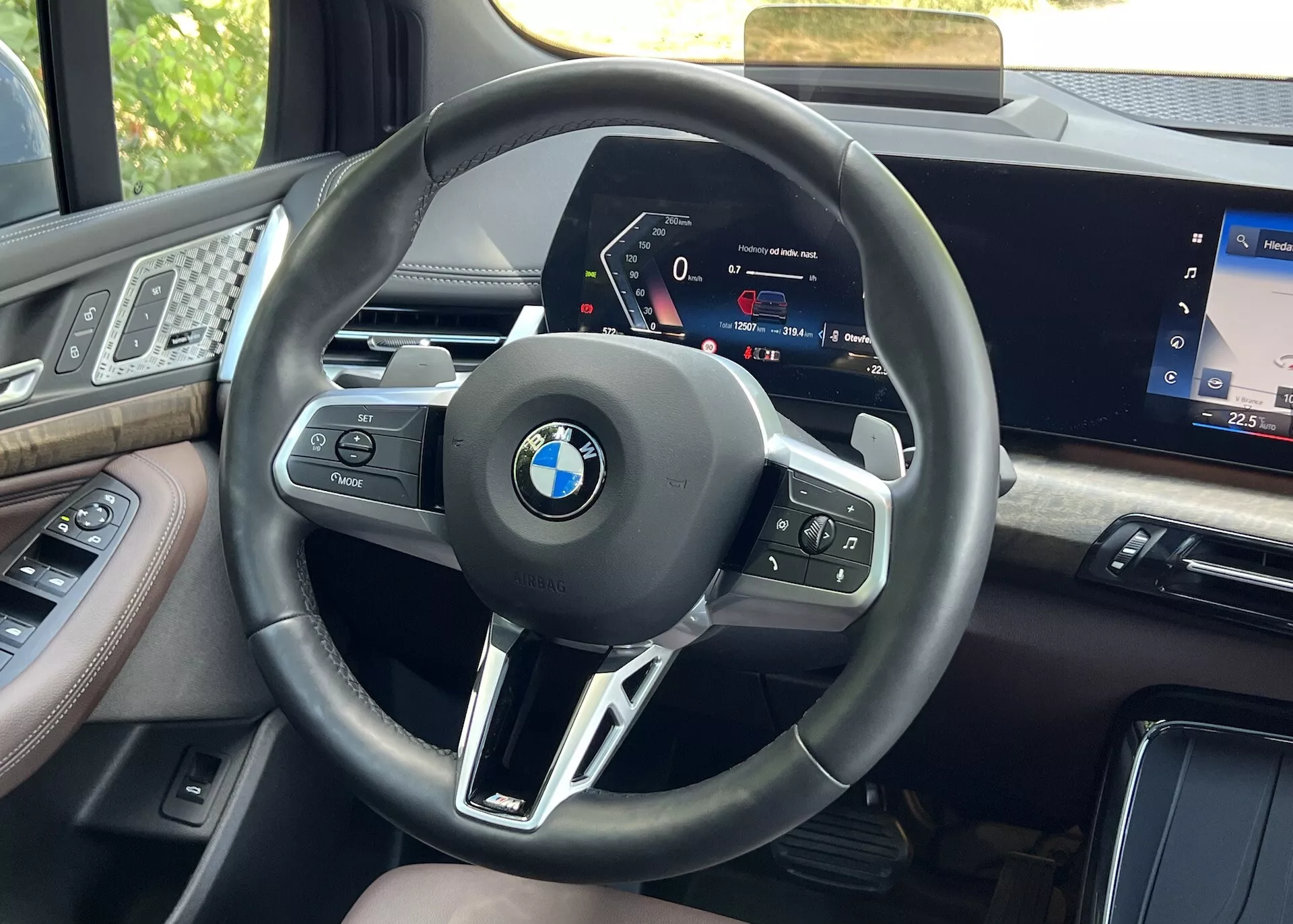 Widok z miejscem kierowcy wnętrza BMW serii 2 Active Gran Tourer z roku 2022, skupiający się na kierownicy z przyciskami wielofunkcyjnymi i wysoko rozdzielczym cyfrowym panelem instrumentów, otoczonym przez materiały premium oraz część ekranu systemu infotainment