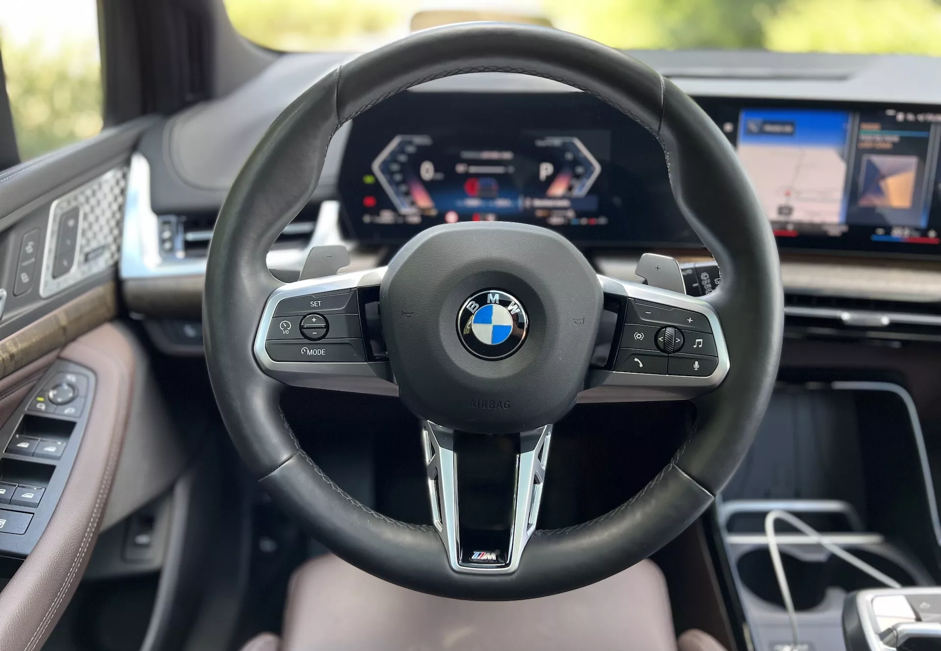 Widok wnętrza BMW 2 Series Active Tourer 2022 z perspektywy kierowcy z widoczną kierownicą z logo BMW i oznaczeniem M, cyfrowym zegarem i częściowym wyświetlaczem systemu infotainment pokazującym zaawansowaną technologię pojazdu i luksusowe funkcje