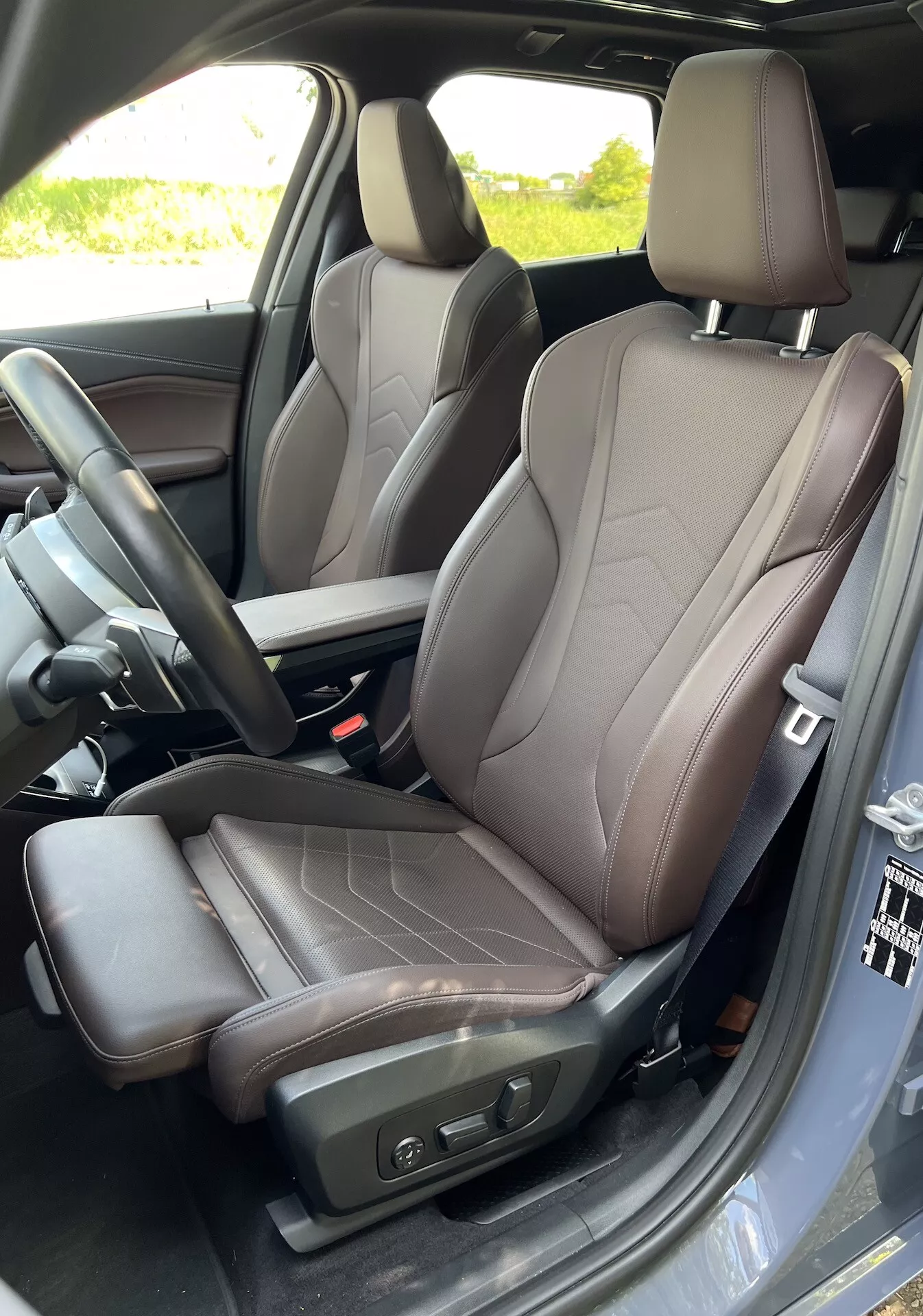 Widok wnętrza na fotel kierowcy BMW Serii 2 Active Gran Tourer 2022, podkreślający nowoczesny design siedzenia z dwukolorową skórą, elektryczne sterowanie regulacji i widoczną część konsoli środkowej