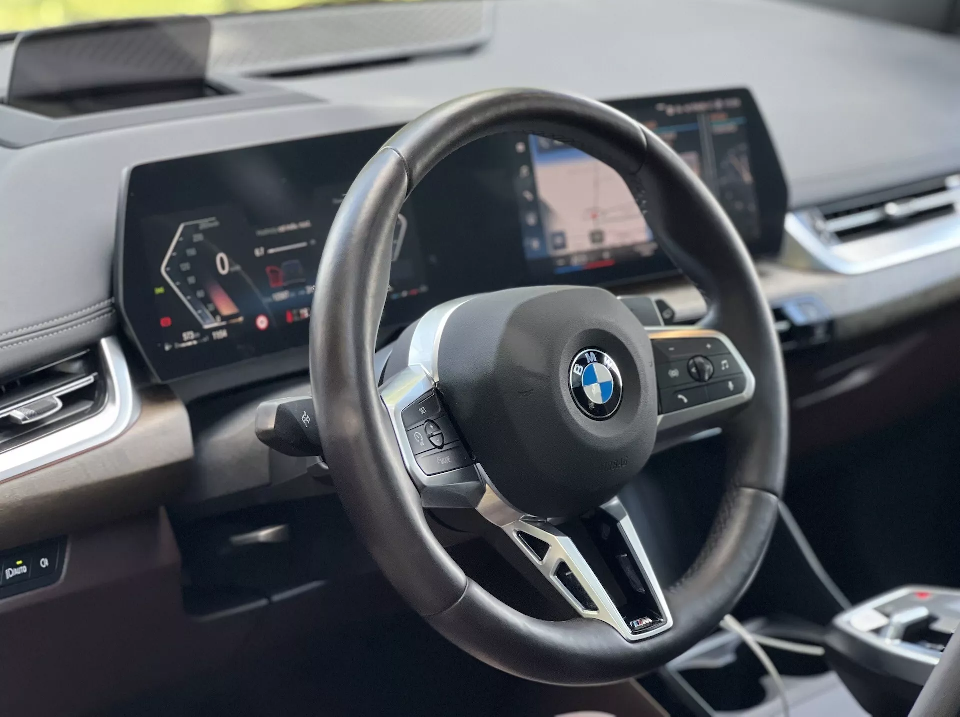 Zdjęcie wnętrza BMW Serii 2 Active Tourer 2022: kierownica z emblematem BMW i elementami wielofunkcyjnymi, cyfrowy kokpit oraz centralny wyświetlacz systemu infotainment z nawigacją, z perspektywy kierowcy