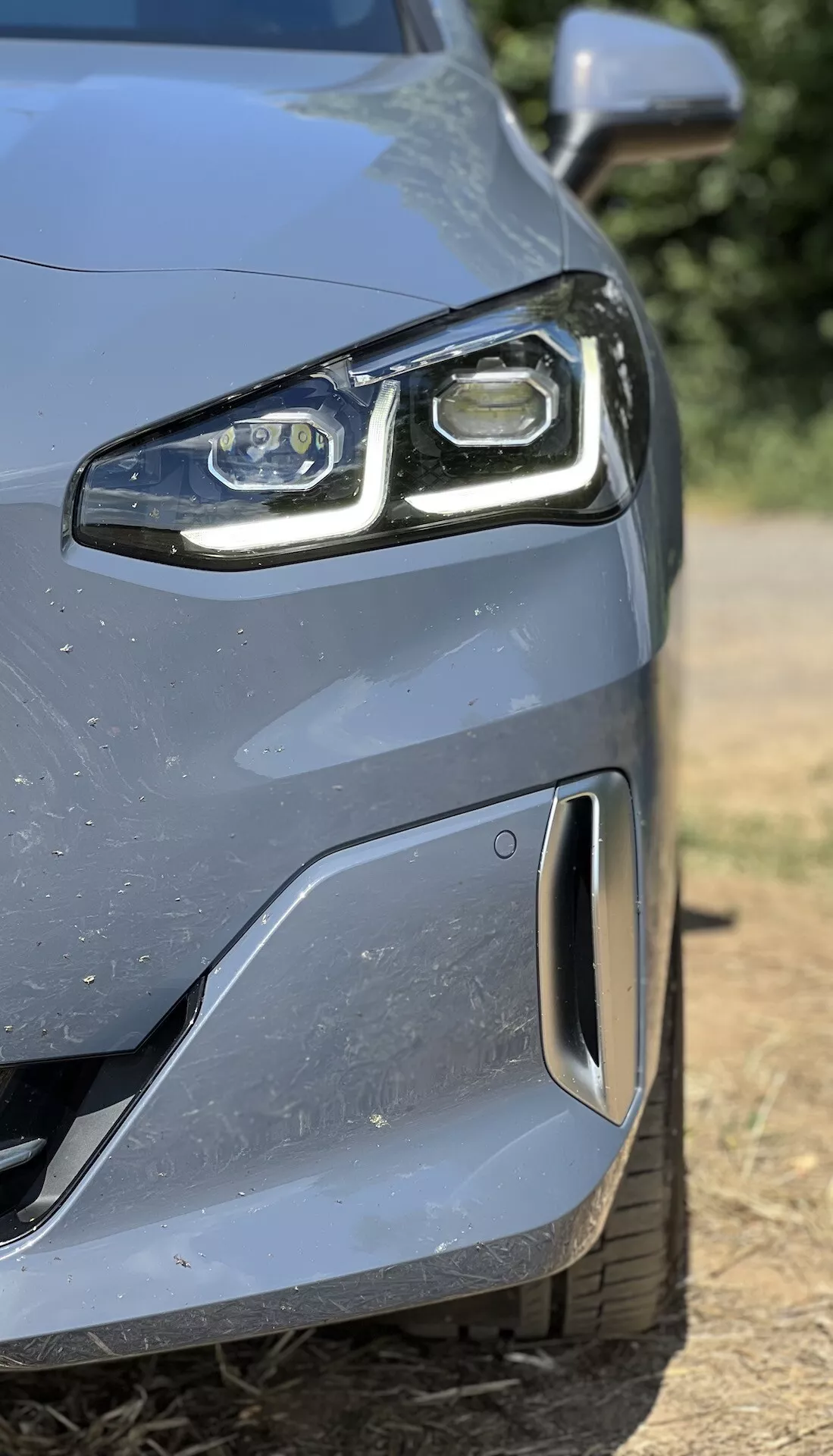 Zbliżenie na przednią lewą stronę BMW serii 2 Active Gran Tourer 2022 z reflektorem LED i aerodynamicznym zderzakiem z czujnikiem parkowania, pokazujące zaawansowaną technologię i design.