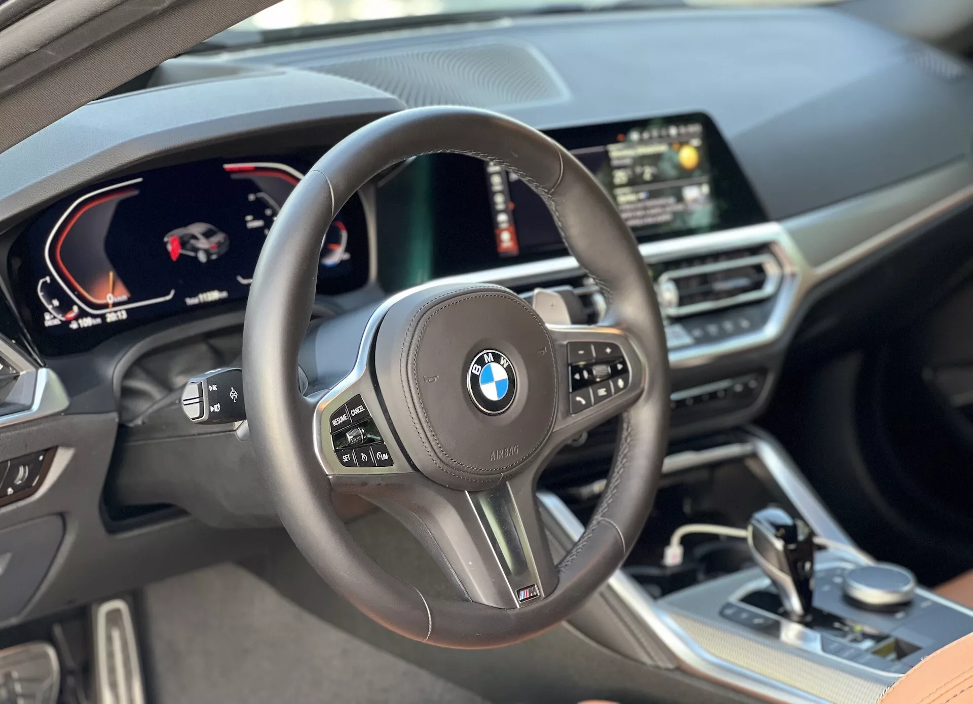 Widok wnętrza BMW Serii 2 Coupé 2022 z perspektywy kierowcy, z centralnie umieszczoną kierownicą z wielofunkcyjnymi przyciskami, cyfrowym zestawem wskaźników pokazującym prędkościomierz i obrotomierz, centralnym cyfrowym wyświetlaczem z nawigacją GPS oraz materiałami wysokiej jakości, w tym skórzanymi powierzchniami i starannie zaprojektowanymi elementami wykończeniowymi w kabinie.