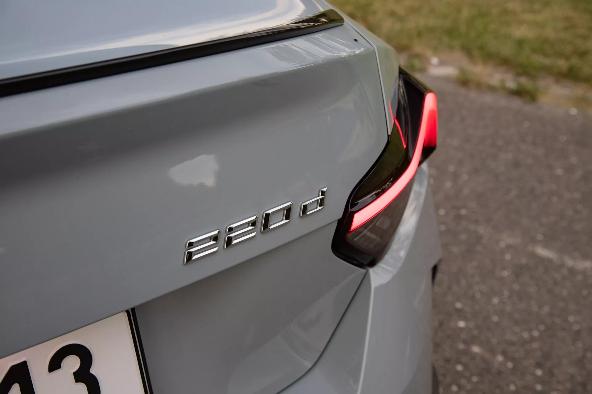 Zbliżenie tylnej prawej sekcji BMW 530d, podkreślające oznaczenie modelu '530d' i skupiające się na nowoczesnym, częściowo podświetlonym tylnym świetle LED. Kolor samochodu to metaliczny srebrny lub szary z delikatnym odbiciem w naturalnym świetle, sugerując wieczorne lub zacienione otoczenie. Emblemat jest chromowany lub metalowy, kontrastujący z lakierem samochodu i umieszczony na klapie bagażnika. Zawiera małą głębię ostrości, która podkreśla emblemat '530d' i pobliską karoserię, jednocześnie rozmywając tło, odpowiednie dla miłośników technologii motoryzacyjnej lub wzornictwa pojazdów.
