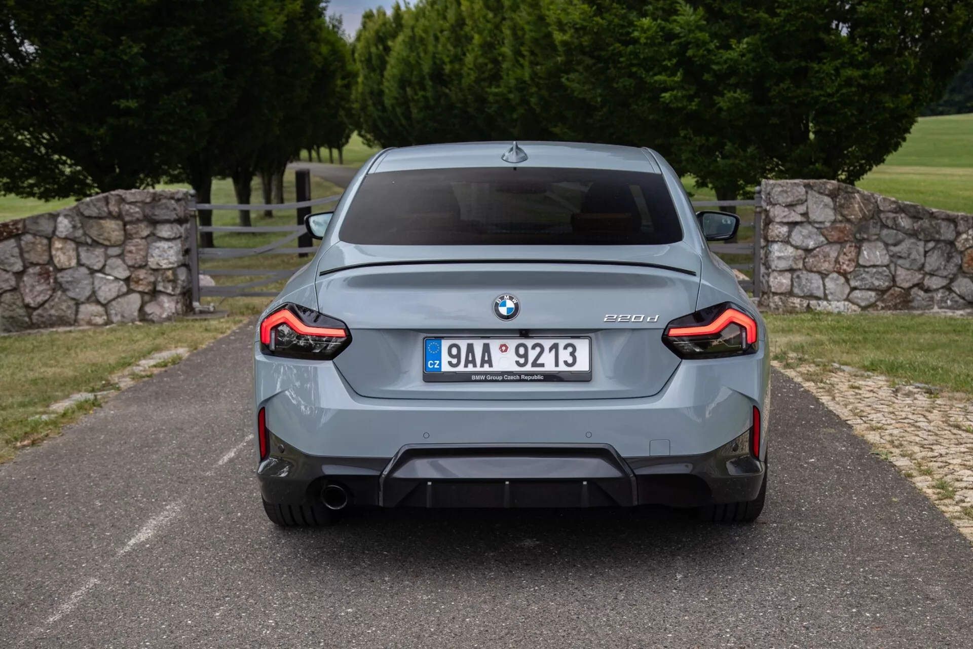 Widok tylni szarego sedana BMW M3 (model G80) z widocznym emblematem BMW, oznaczeniem modelu M3 z informacjami o modelu G80, centralną tablicą rejestracyjną, sportowym tylnym zderzakiem z wbudowanym dyfuzorem, podwójnymi końcówkami wydechu, pełnowymiarowymi tylnymi lampami LED w kształcie litery L oraz poszerzonymi nadkolami.