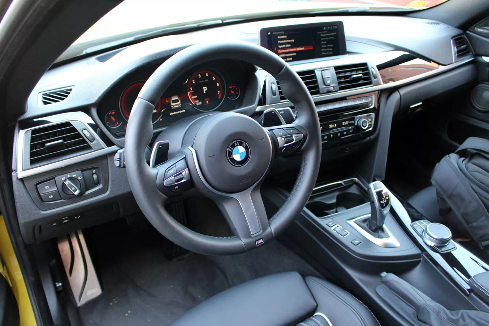 Widok wnętrza BMW serii 4 Coupe z 2013 roku z perspektywy kierowcy pokazujący kierownicę, deskę rozdzielczą, konsolę środkową z kontrolami multimedialnymi i klimatyzacji, dźwignię zmiany biegów i luksusowe wykończenia
