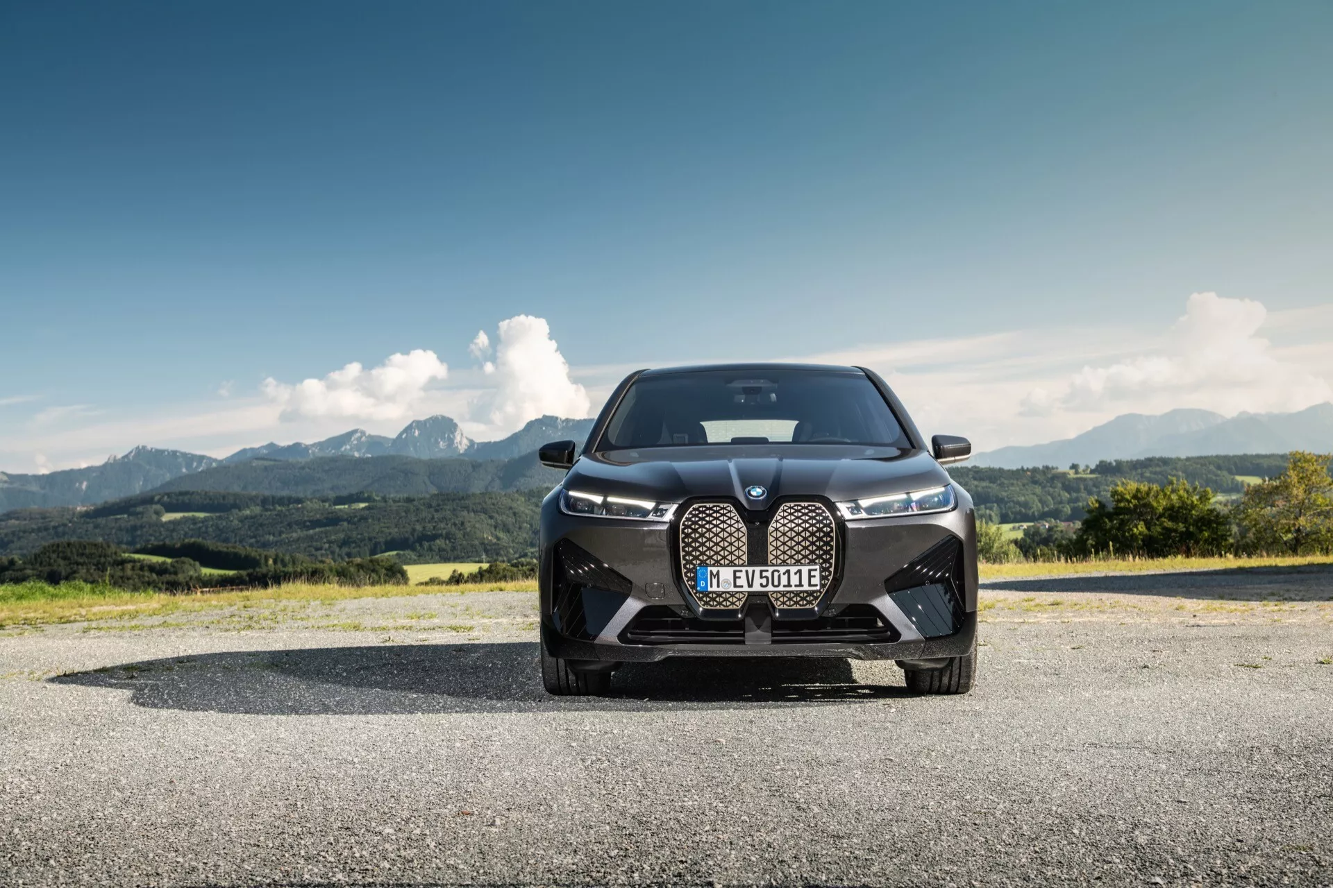 BMW iX (i20) 2021 sfotografowane z niskiej perspektywy czołowej, podkreślające jego dominujący design z dużym grillem nerkowym, smukłymi reflektorami LED i wlotami powietrza zorientowanymi na wydajność na tle górskiego krajobrazu