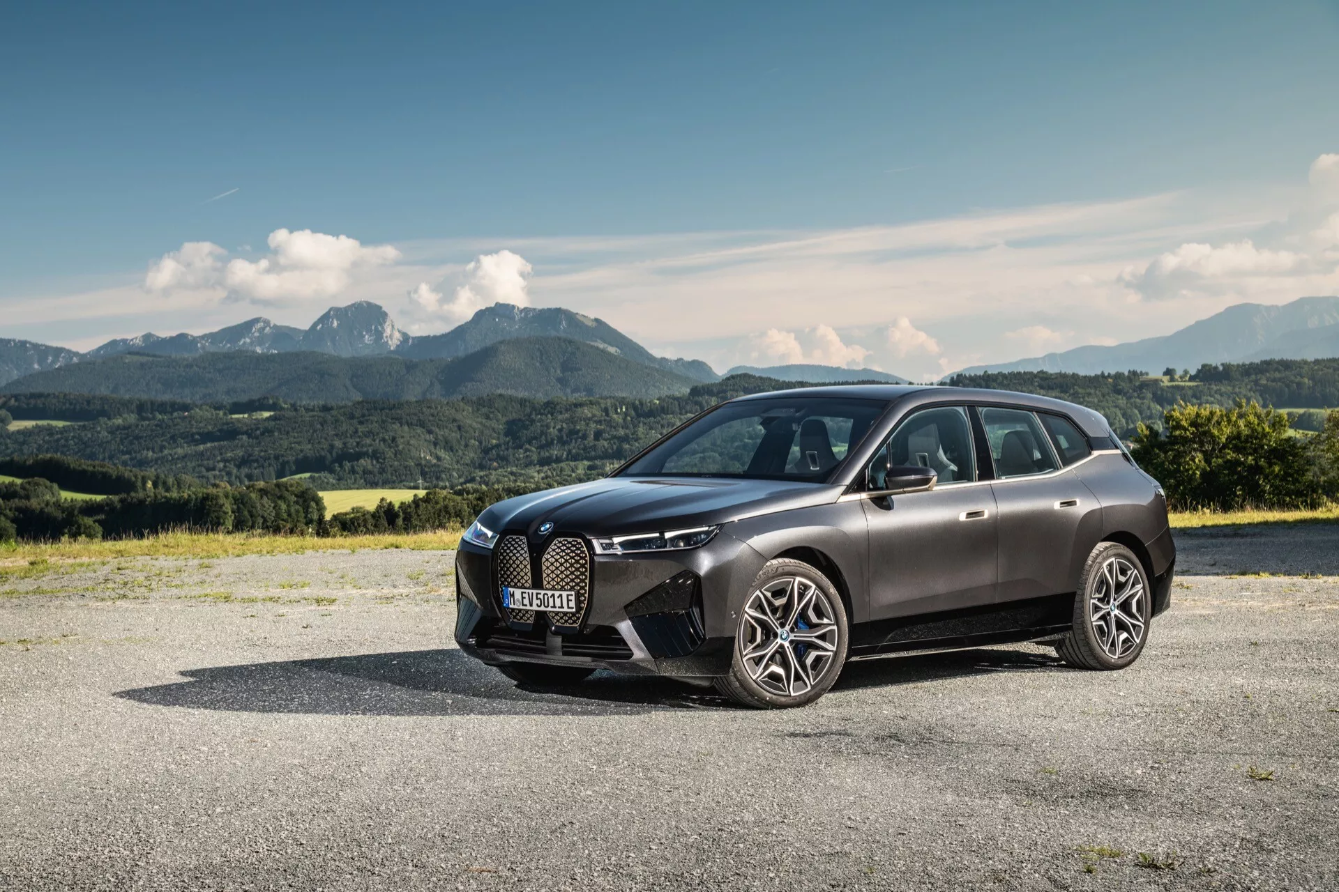 Luksusowy SUV BMW iX (i20) z 2021 roku zaparkowany na zewnątrz, prezentujący swój nowoczesny design na tle malowniczego krajobrazu górskiego, podkreślający przedni grill, światła LED i elegancką, aerodynamiczną karoserię