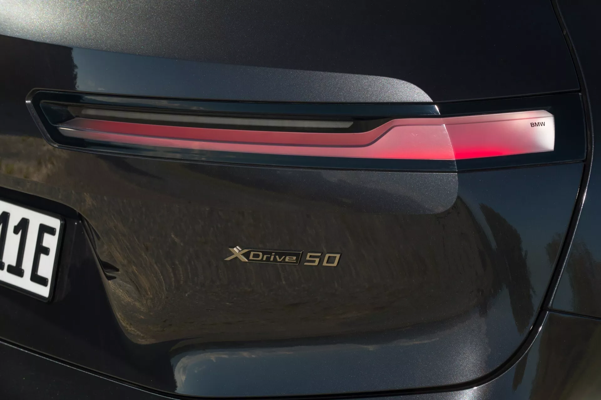 Zbliżenie na tylną część BMW iX 2021 (i20) podkreślające diodowe światło tylne, odznakę xDrive 50 i wysoki połysk
