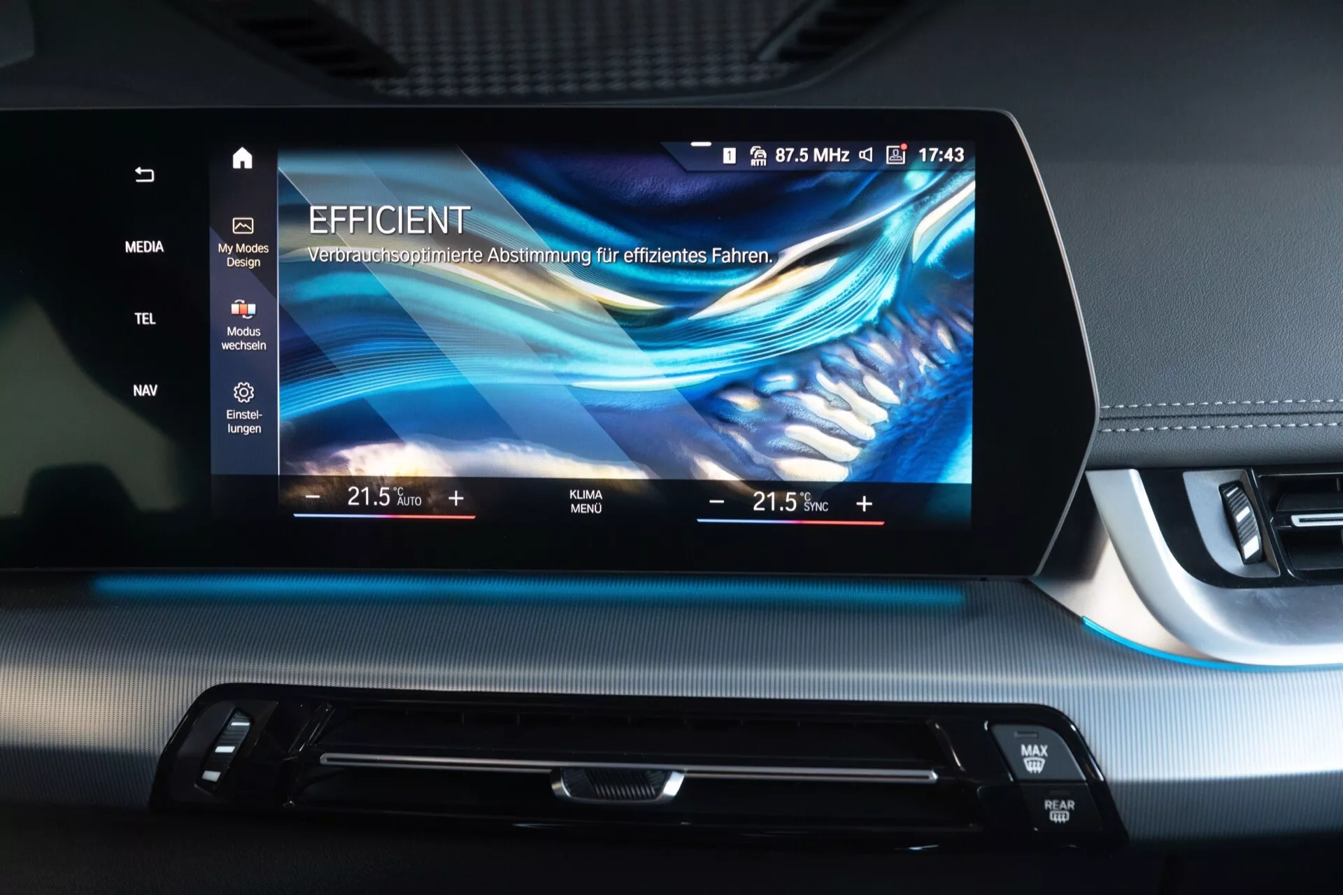 Wnętrze deski rozdzielczej BMW iX1 2022 (U11) z centralnym dotykowym wyświetlaczem infotainment oznaczonym 'EFFICIENT' z niemieckim tekstem o optymalizacji zużycia, eleganckimi fizycznymi przyciskami sterowania klimatyzacją, ustawieniami klimatyzacji dwustrefowej na 21,5°C, materiałami wysokiej jakości i oświetleniem ambientowym.