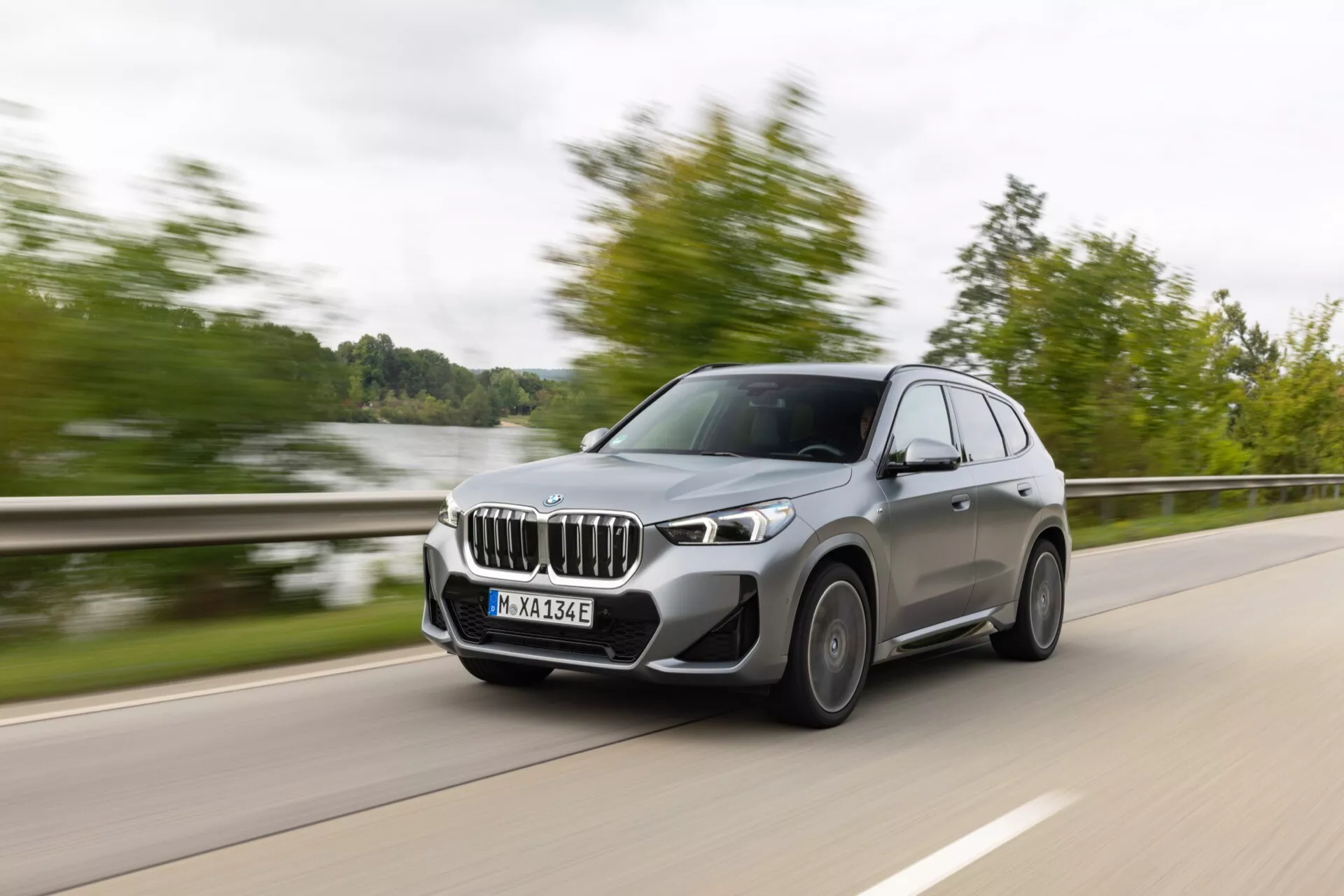 Dynamiczny widok z boku nowoczesnego średniej wielkości luksusowego SUV-a w ruchu, z BMW X3 z elektryfikowanym układem napędowym, podkreślający charakterystyczne nerki, światła do jazdy dziennej LED, aluminiowe felgi i zaawansowane technologie asystujące kierowcy uchwycone za pomocą techniki fotografii panoramicznej.