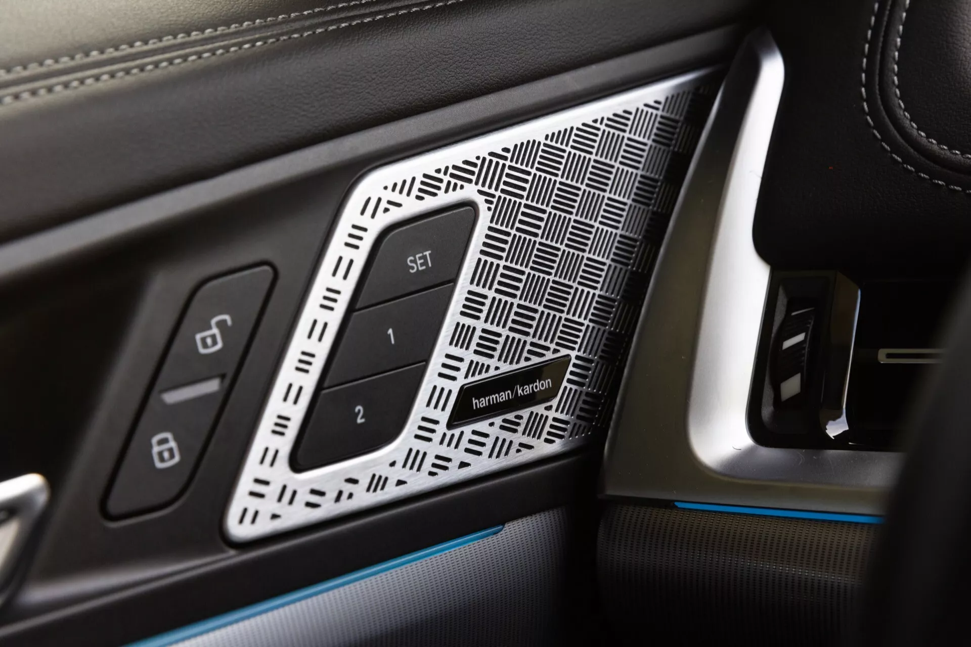 Zbliżenie na panel drzwi kierowcy w BMW X1 2022 (U11), przedstawiający detale wykończenia luksusowego, takie jak skóra z kontrastowym szwem, wstawka geometryczna, przyciski pamięci ustawień fotela i oświetlenie ambientowe