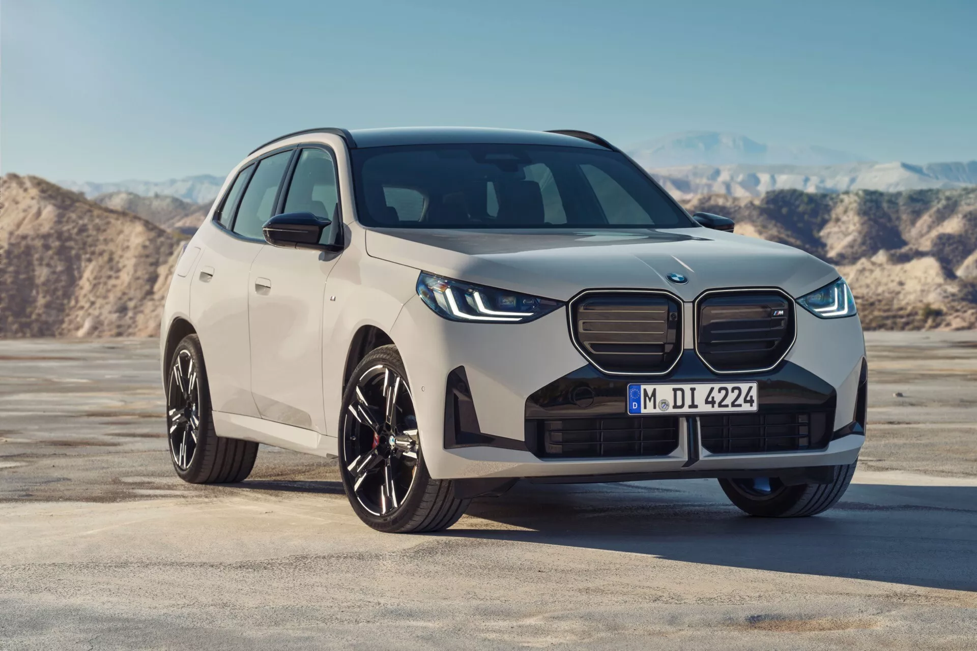 Profesjonalne zdjęcie BMW X3 2024 (G45) z przedniego trzech czwartych kąta, ukazujące przód samochodu, wyrazistą kratkę, ostre reflektory LED, stylowe felgi aluminiowe i elegancki boczny profil. Uchwycony z matowym/satynowym wykończeniem, SUV prezentuje nowoczesny, premium design z potencjalnymi zaawansowanymi technologiami wspomagania kierowcy, na tle pustego, płaskiego terenu.