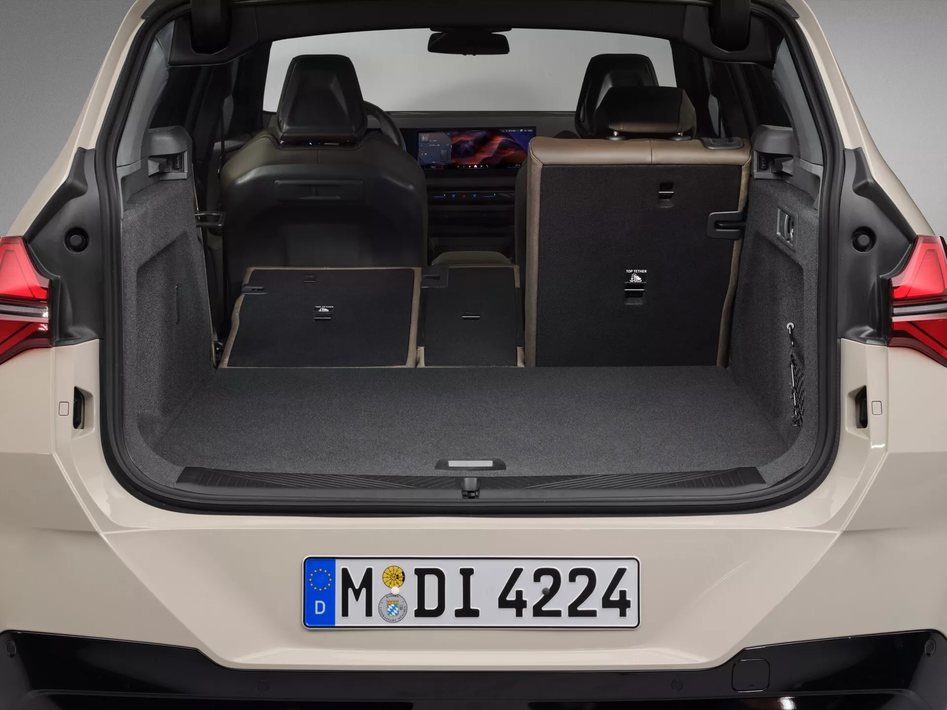 Tylne wnętrze BMW X3 2024 (G45) widziane od tyłu, koncentrujące się na przestronnej pustej przestrzeni ładunkowej; tylne siedzenia złożone na płasko w celu zwiększenia pojemności ładunkowej; ciemne wnętrze kontrastujące z jaśniejszą farbą zewnętrzną; cechy obejmują punkty mocowania dla bezpiecznego transportu, boczne schowki i uchwyt ręczny do zamykania bagażnika; potencjalne oświetlenie bagażnika i ukryte gniazdo 12V.
